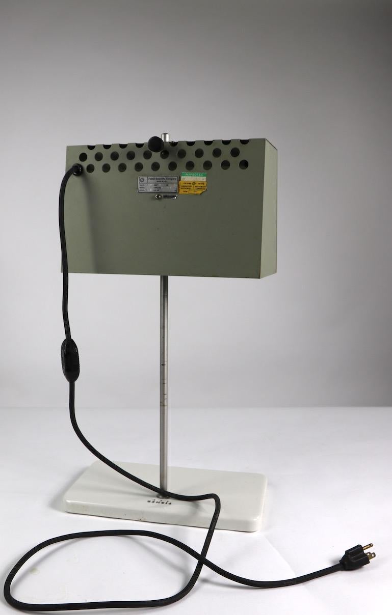 Fisher scientific lamp, having an adjustable metal box shade with perforated holes. Shade 12.5 W x 8 H x 6 D inches. Shade will raise, lower, and pivot to adjust light direction. Shade mounts to metal rod, which rests on white ceramic base. Base 13