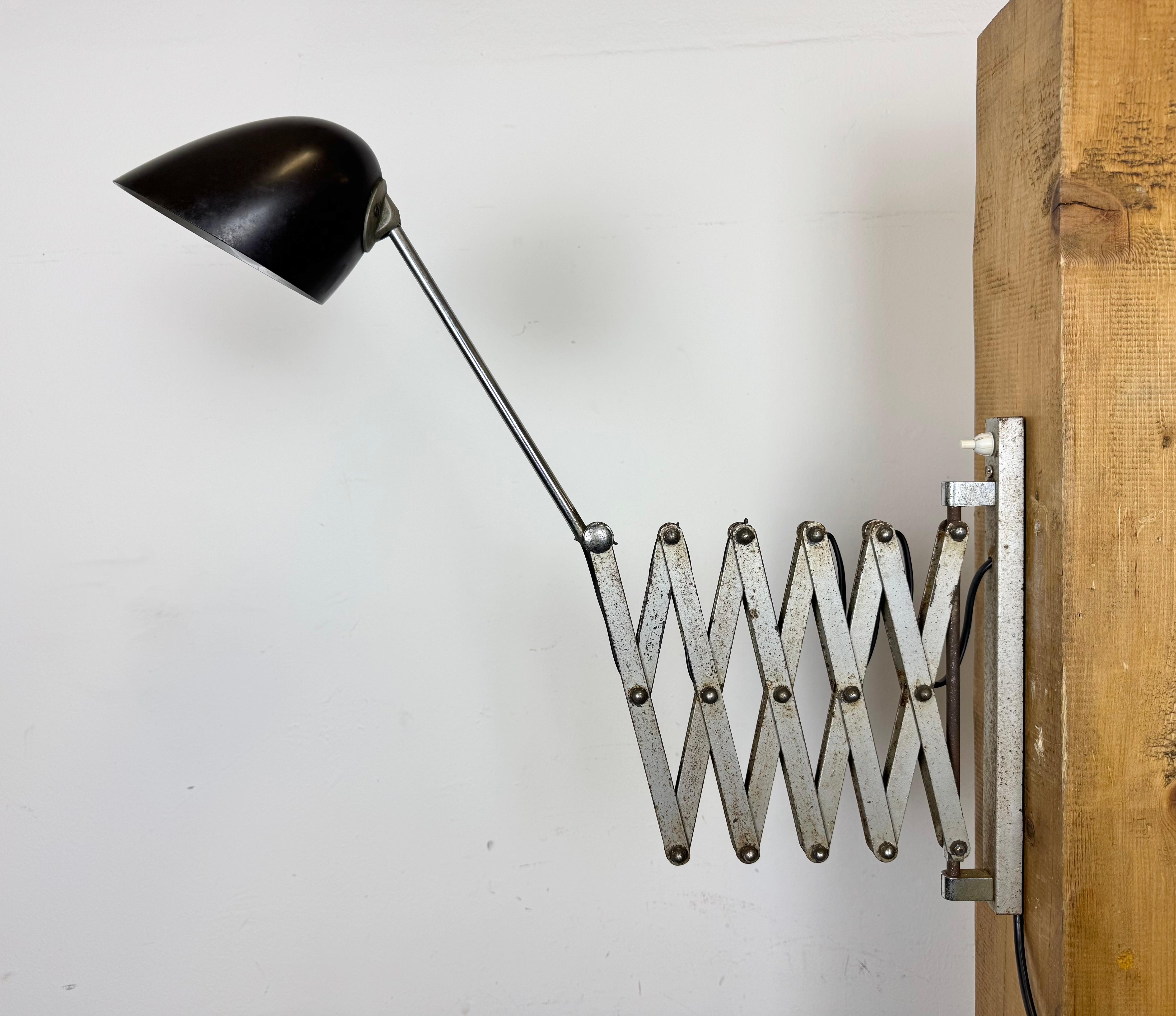 Cette applique industrielle vintage à ciseaux réglables a été produite dans l'ancienne Tchécoslovaquie au cours des années 1950. La lampe a un abat-jour en bakélite marron. Le bras en ciseaux en fer chromé est extensible et peut être tourné sur le