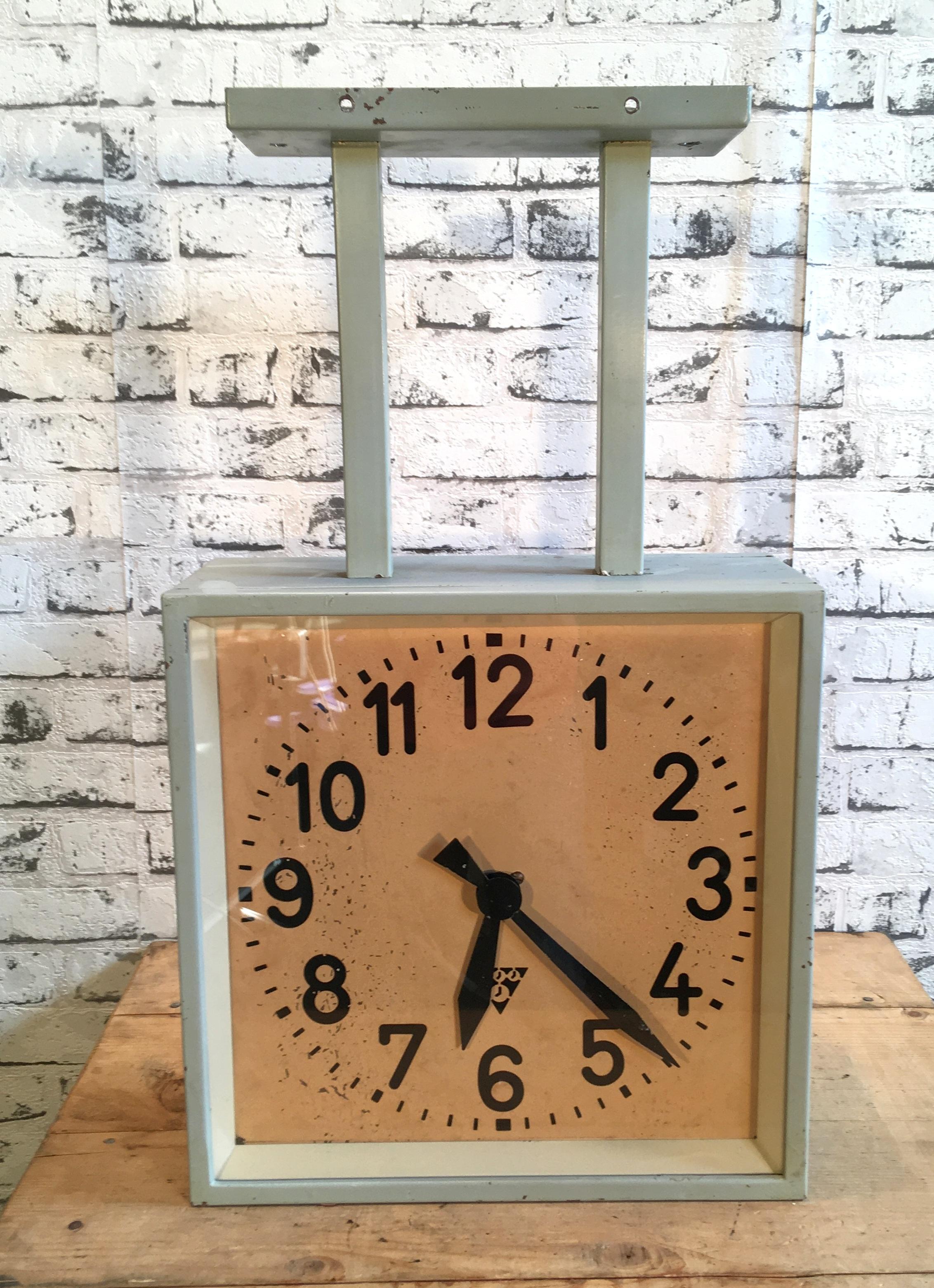 This square double-sided railway or factory clock was produced by Pragotron, in former Czechoslovakia, during the 1950s. The piece features a grey metal body and a clear glass cover. The clock has been converted into a battery-powered clockwork and