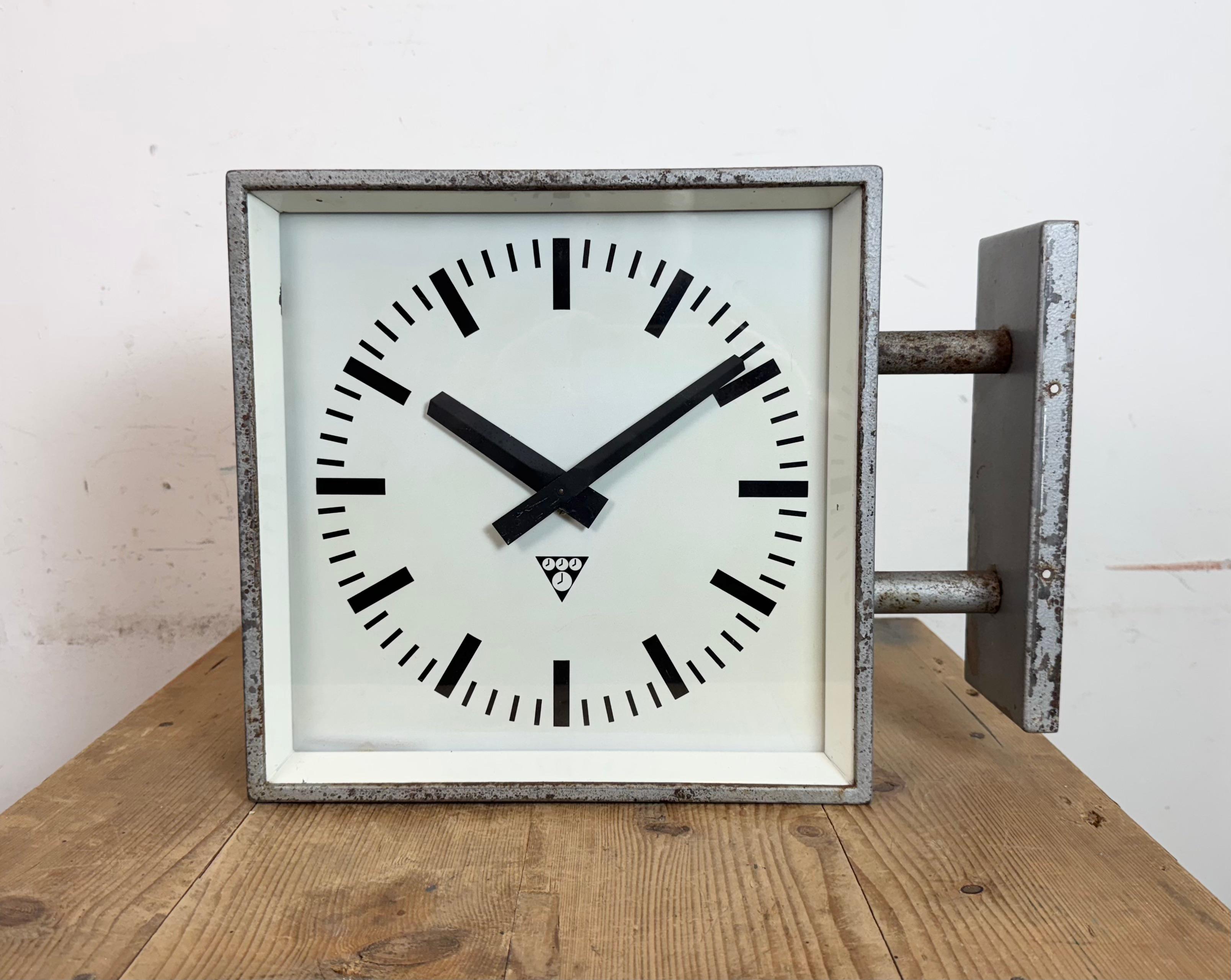 Diese quadratische, doppelseitige Wanduhr für Eisenbahnen, Schulen oder Fabriken wurde in den 1970er Jahren von Pragotron in der ehemaligen Tschechoslowakei hergestellt. Die Uhr besteht aus einem grauen Metallgehäuse, einem grauen Uhrenrahmen, einer