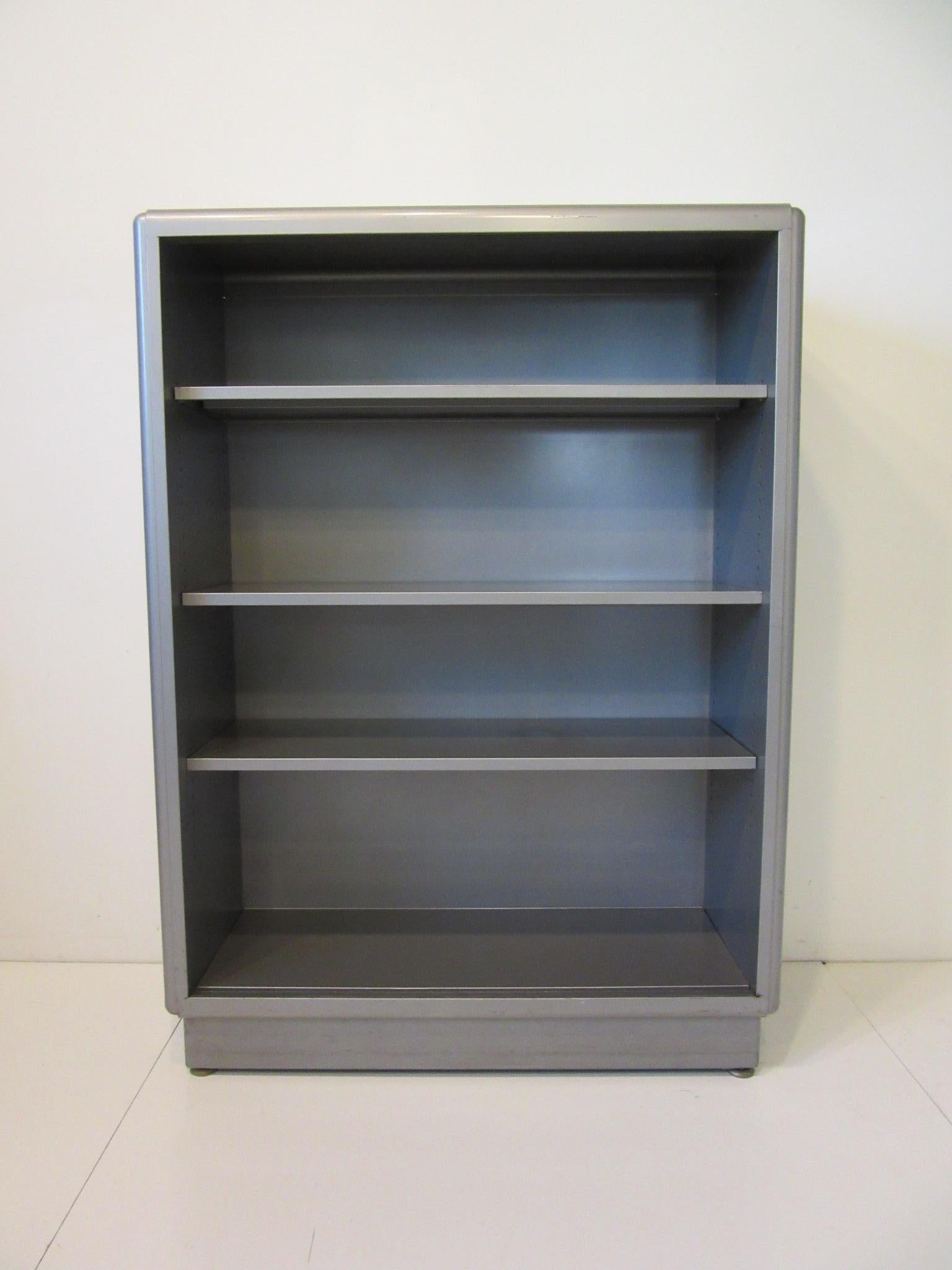 A nice streamline industrial metal bookcase in a medium gray with three adjustable matching shelves having two sliding glass doors with grooved handles in the glass. Retains the original manufactures label by ASE The All Steel Equipment Company and