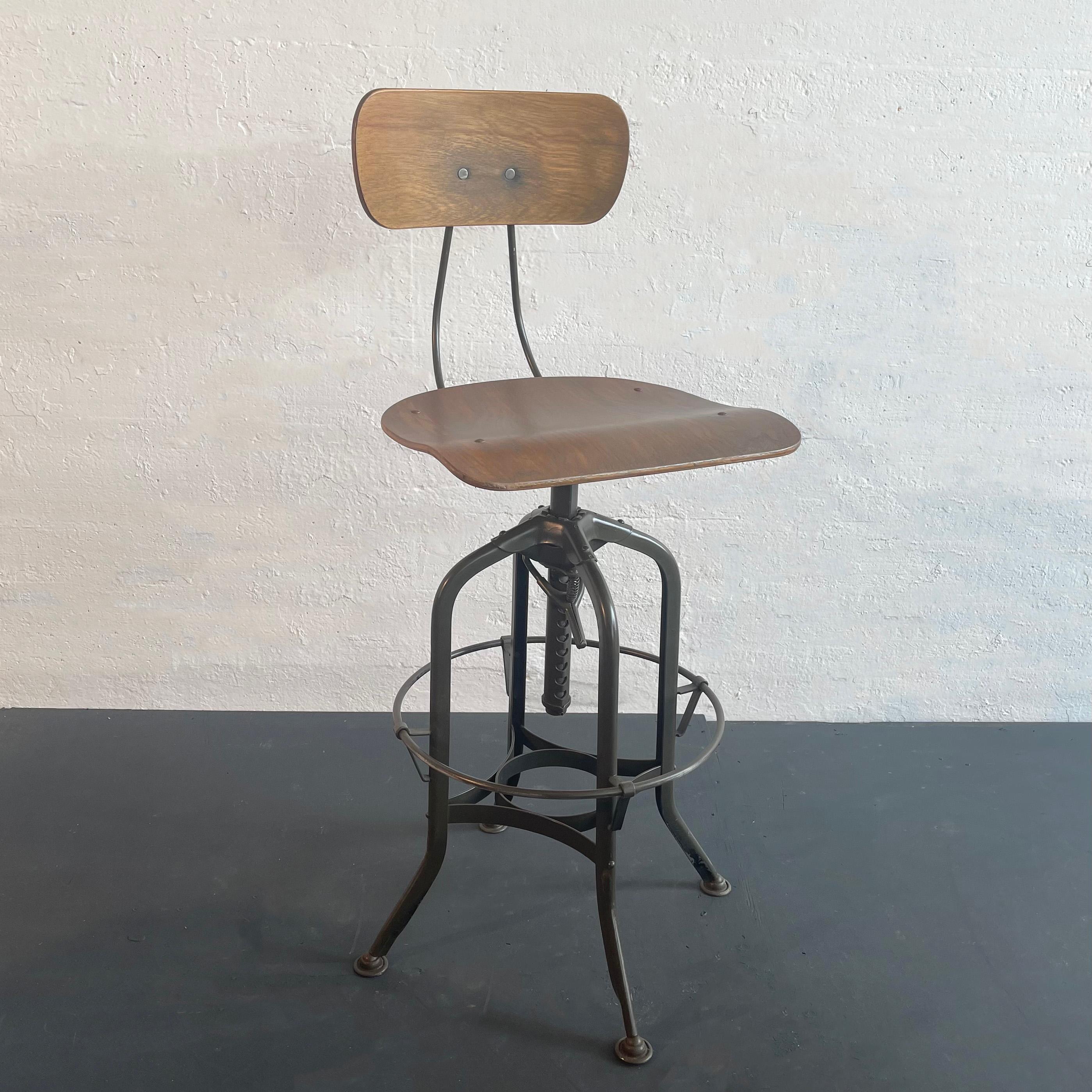 Iconic, vintage, industrial drafting stool by Toledo Metal Furniture Co. circa 1940's features a refinished bent ply, potato chip seat and back that swivels on a painted steel, star base with a 15.5 inch diameter foot rest at 12 inches height. The