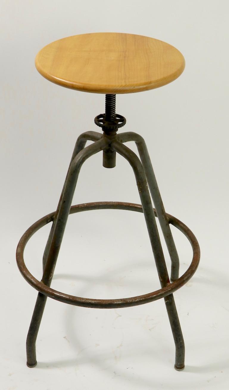 Classic industrial stool with solid wood disk seat, on four tubular steel legs. The seat swivels and is adjustable in height from lowest position 27 to highest position 31 inches. Clean, original, ready to use condition. Diameter of seat 14 inches.
