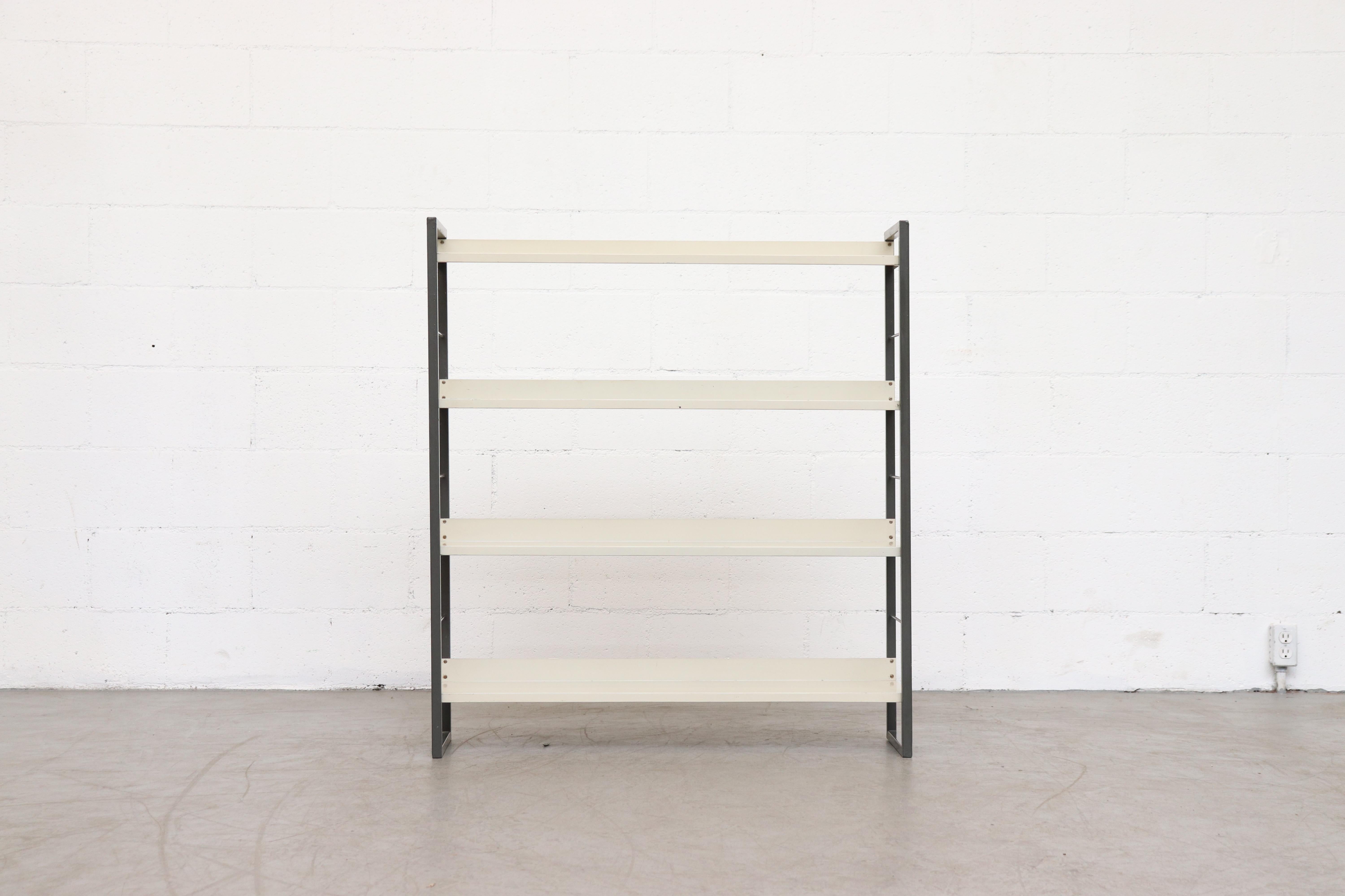 Industrial Tomado enameled metal shelving unit. Charcoal grey enameled metal frame with 4 ivory sheet metal shelves. In good original condition with visible signs of wear including minimal denting, scratching and surface rust, all consistent with