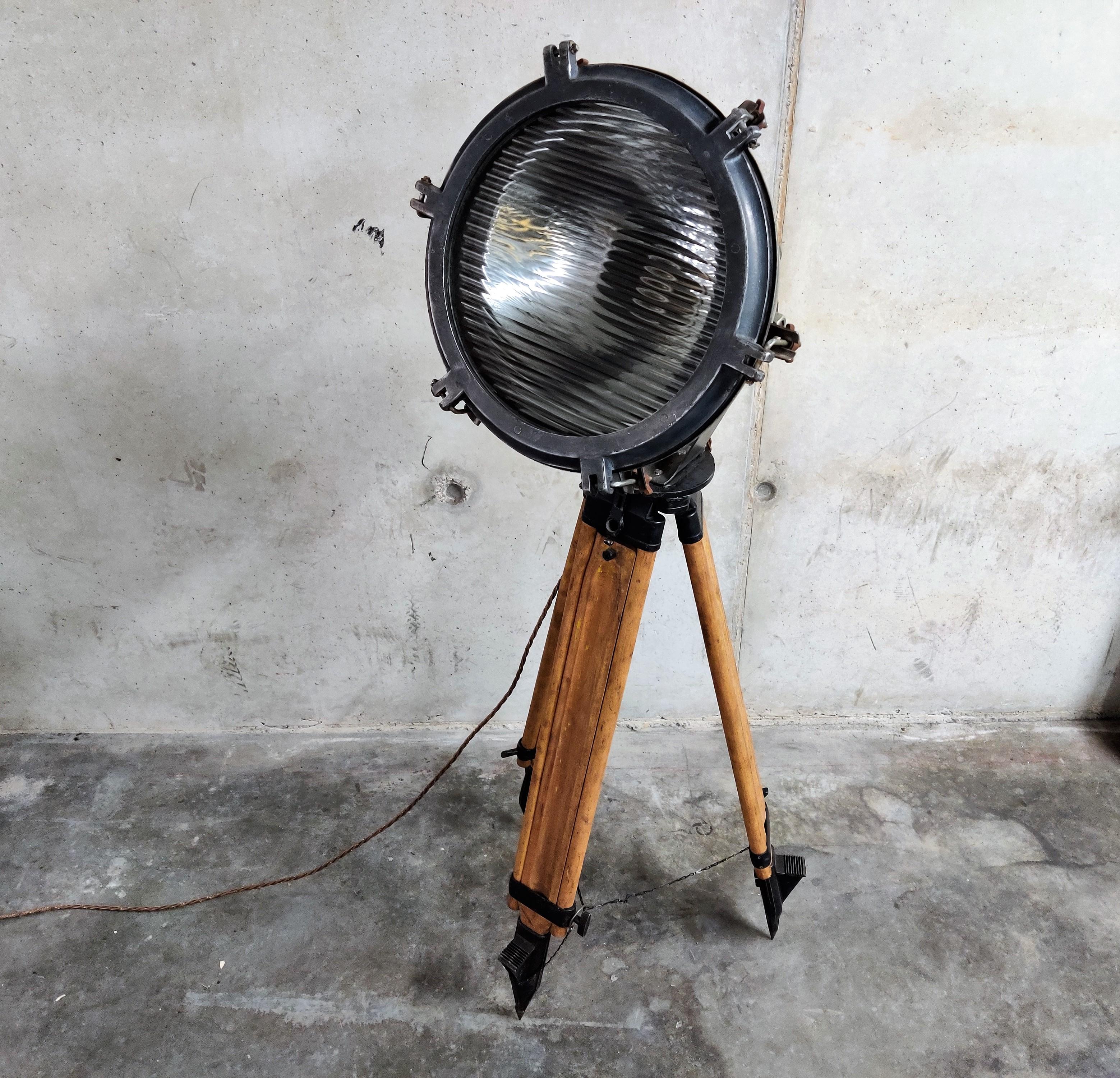 Wonderful industrial spotlight, coming from a ship.

The light has a reflector on the inside and ribbled glass, creating a diffuse light.

The lamp is mounted on a vintage wooden tripod, adjustable in height.

This floor lamp is a real eyecatcher,