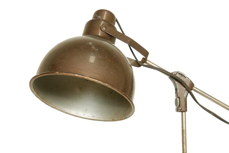 Industrial floor lamp with tripod base and adjustable shade and arm.

USA, circa 1940.

Features:
*Bronze colored shade
*Brushed steel metal arms and base
*Adjustable shade and arm position 
*Adjustable height
*Black spherical accent cap on