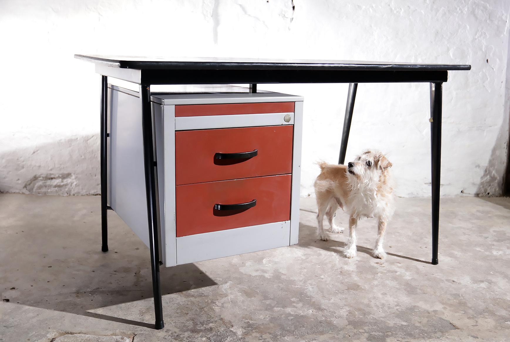 This (probably Dutch design) desk from the 1950s is made of metal with a beautiful sleek design.
The drawers were once painted red, the bottom one was originally yellow and the one above was light gray.
The tabletop is black linoleum with wear