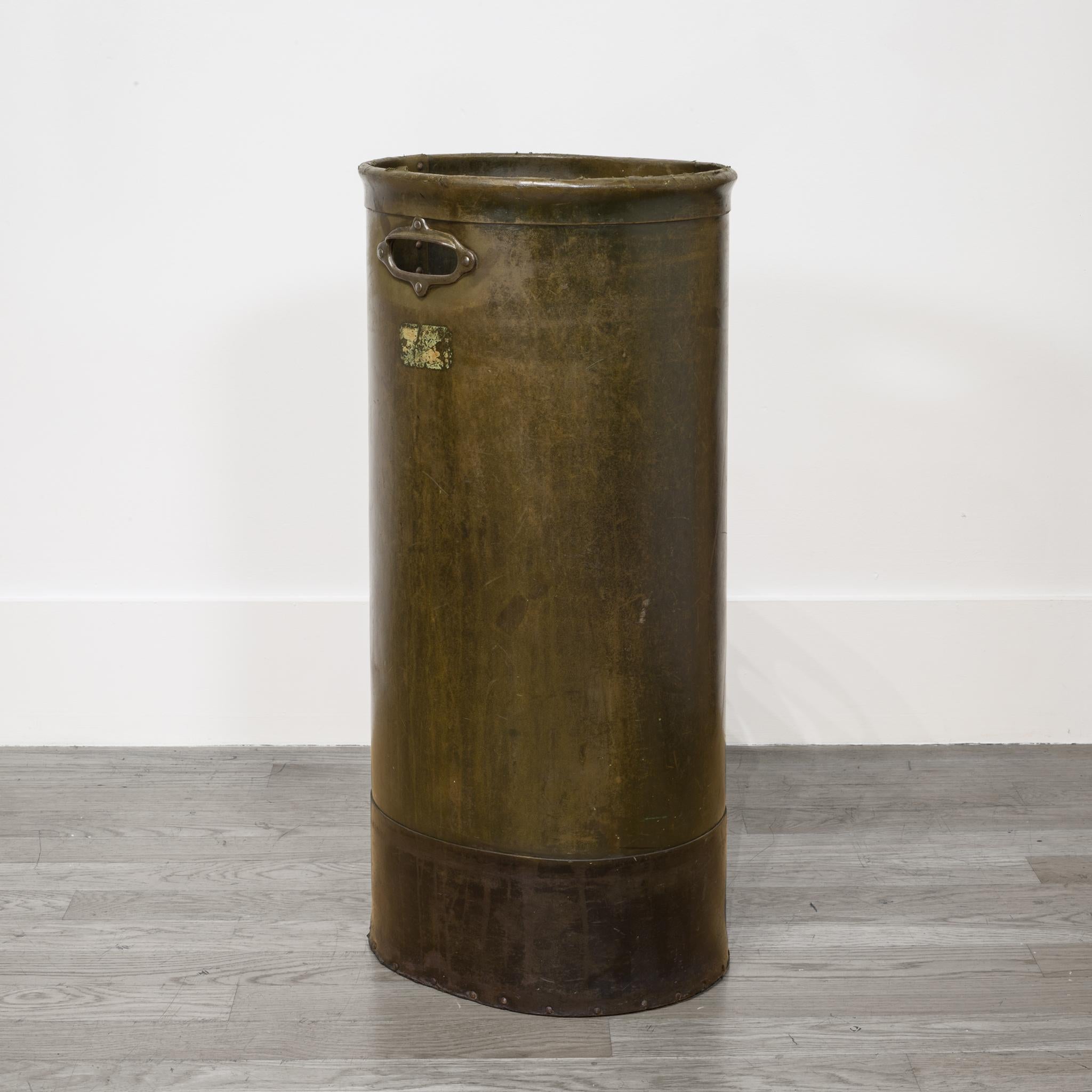 This is an original industrial vulcanized fiber tall waste basket with riveted sides, steel rimmed cutout handles and a rare wooden bottom. There is an original label on one side. This piece has retained its original finish and has the appropriate