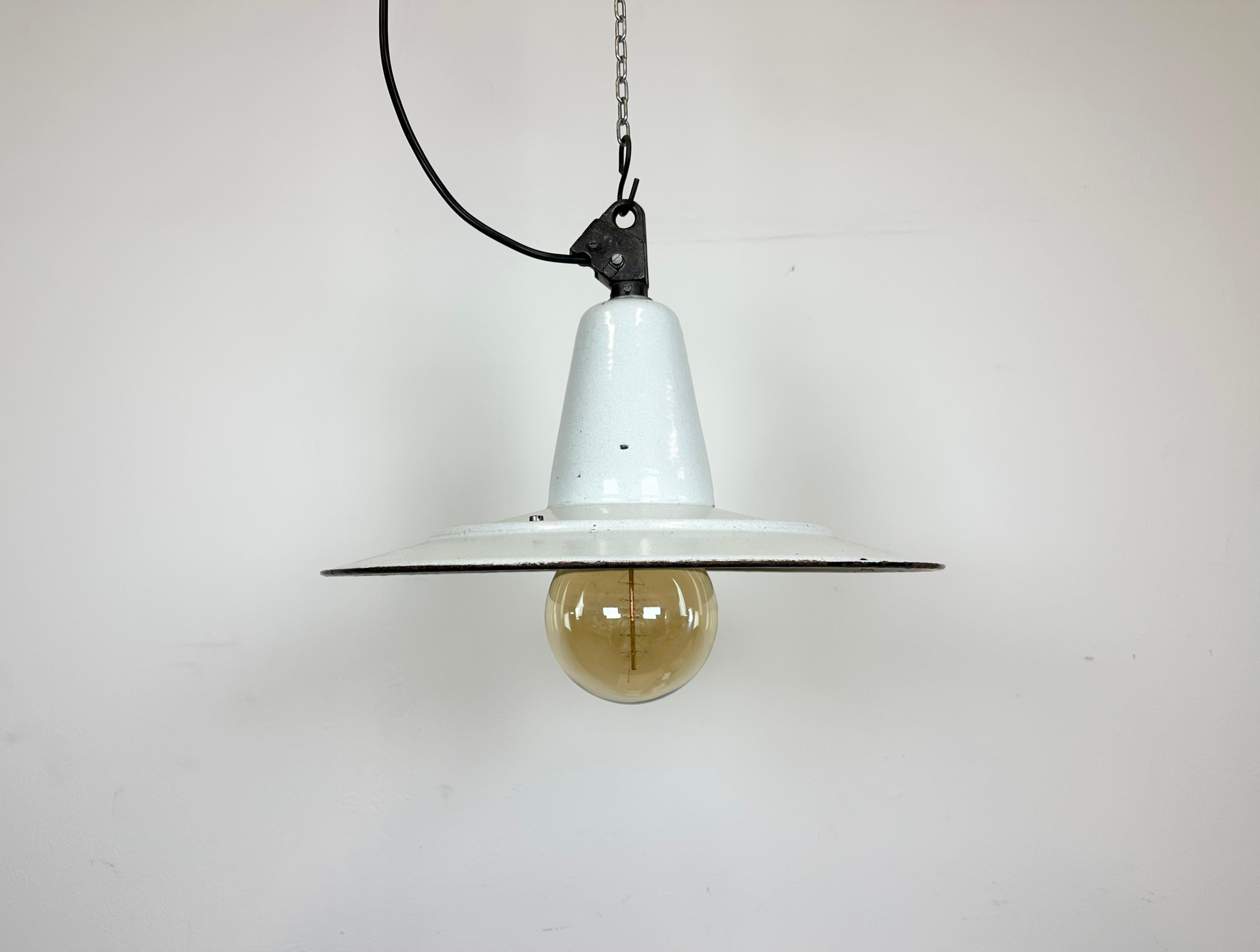 Industrial dark white (light grey) enamel pendant light made in Poland during the 1960s. White enamel inside the shade. Cast iron top. The porcelain socket requires E 27/ E 26 light bulbs. New wire. Fully functional. The weight of the lamp is 2 kg.