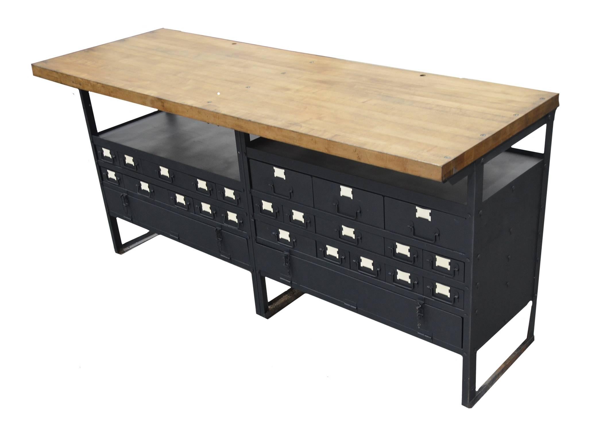 Industrial work table which has been restored for use as a console or center island. Repainted in a dark ink color which reads black / blue with a stained maple wood top. This piece offers great storage with 23 drawers in various sizes as well as