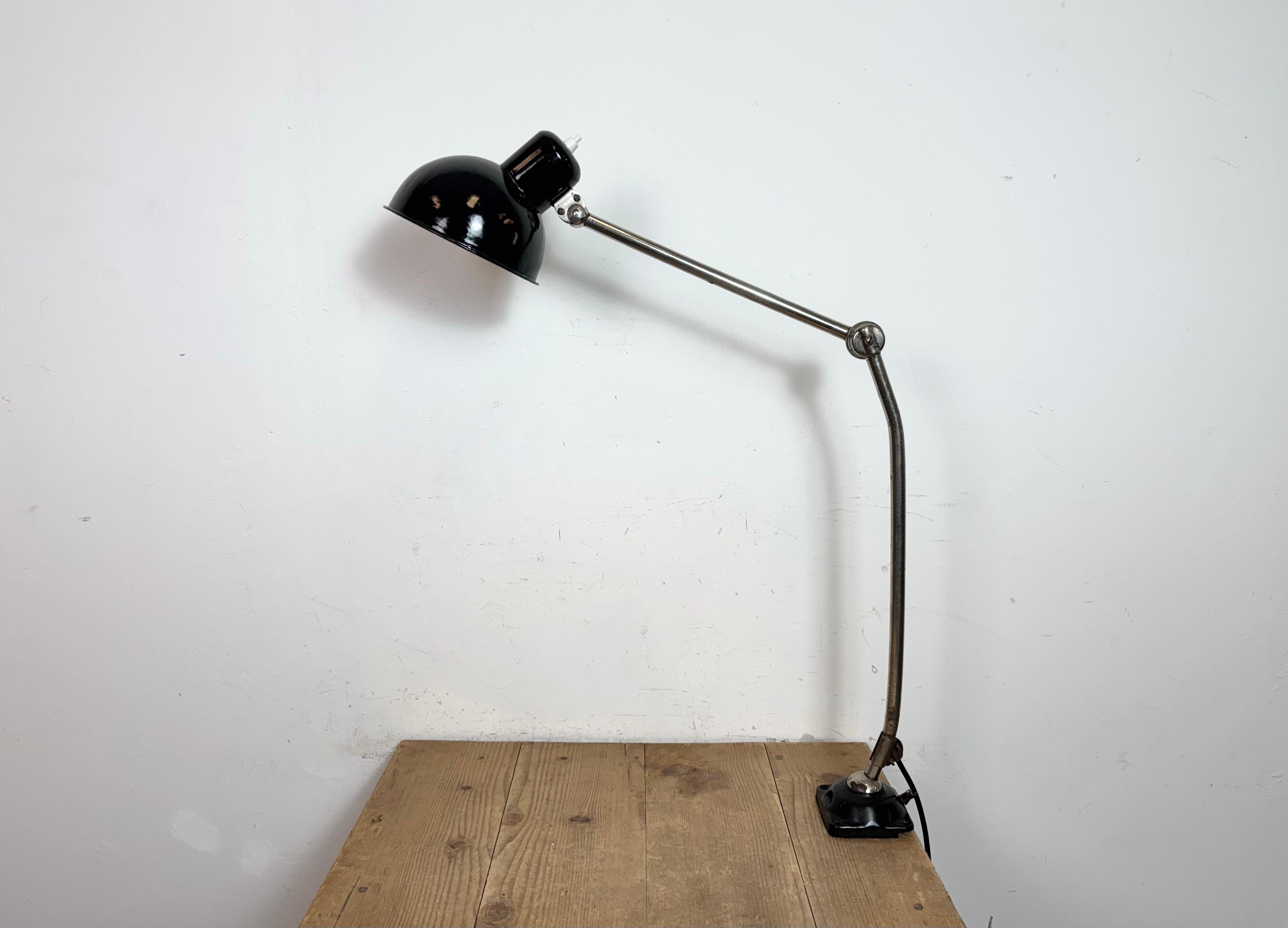 Lampada da tavolo industriale realizzata nell'ex Cecoslovacchia negli anni '50. Presenta un paralume in smalto nero con interno in smalto bianco, una base in ferro e un braccio cromato con tre snodi regolabili. L'interruttore si trova direttamente