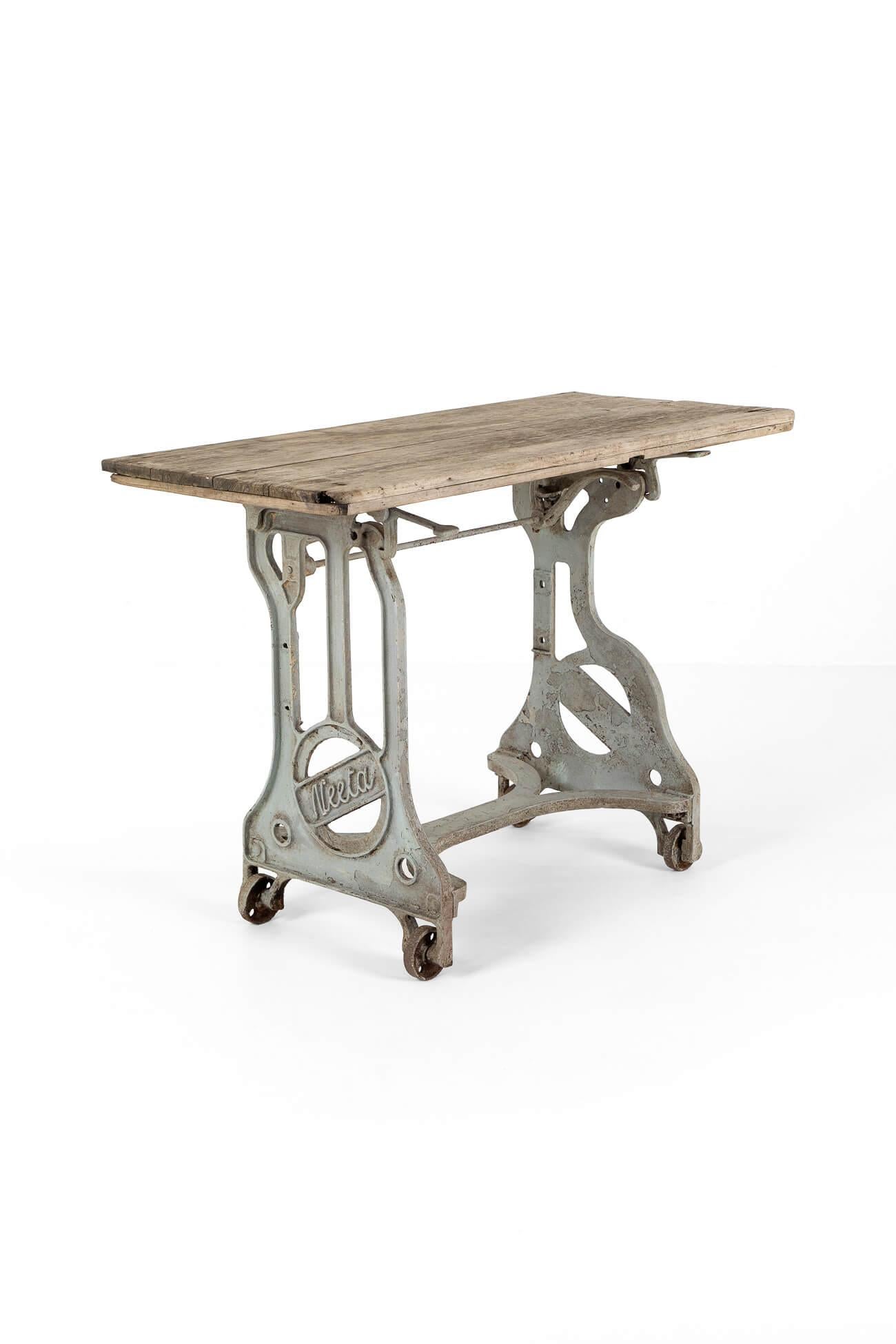 A superb industrial worktable by the manufacturing company Neeta.

The table top of silvered oak is perfectly weathered and attached to the cast iron base with two large bracket hinges. A catch on the base releases the bracket, allowing the tabletop