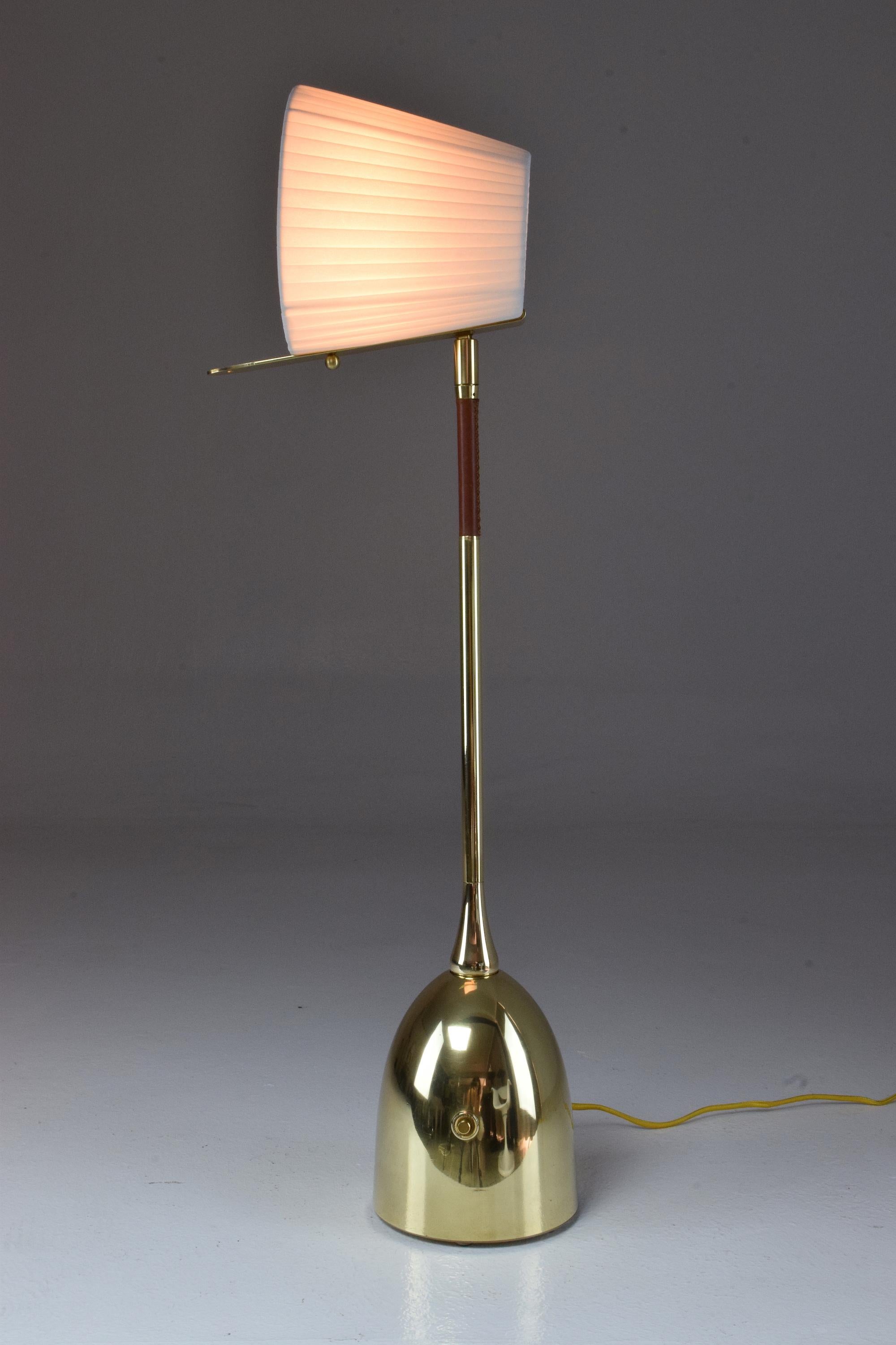 Contemporary handcrafted tall articulating table lamp pictured in a polished brass finish, adorned with a brown hand-sewn sheathed leather detail and designed with our signature pear shaped joint . The shade is built with a stem so you can orientate