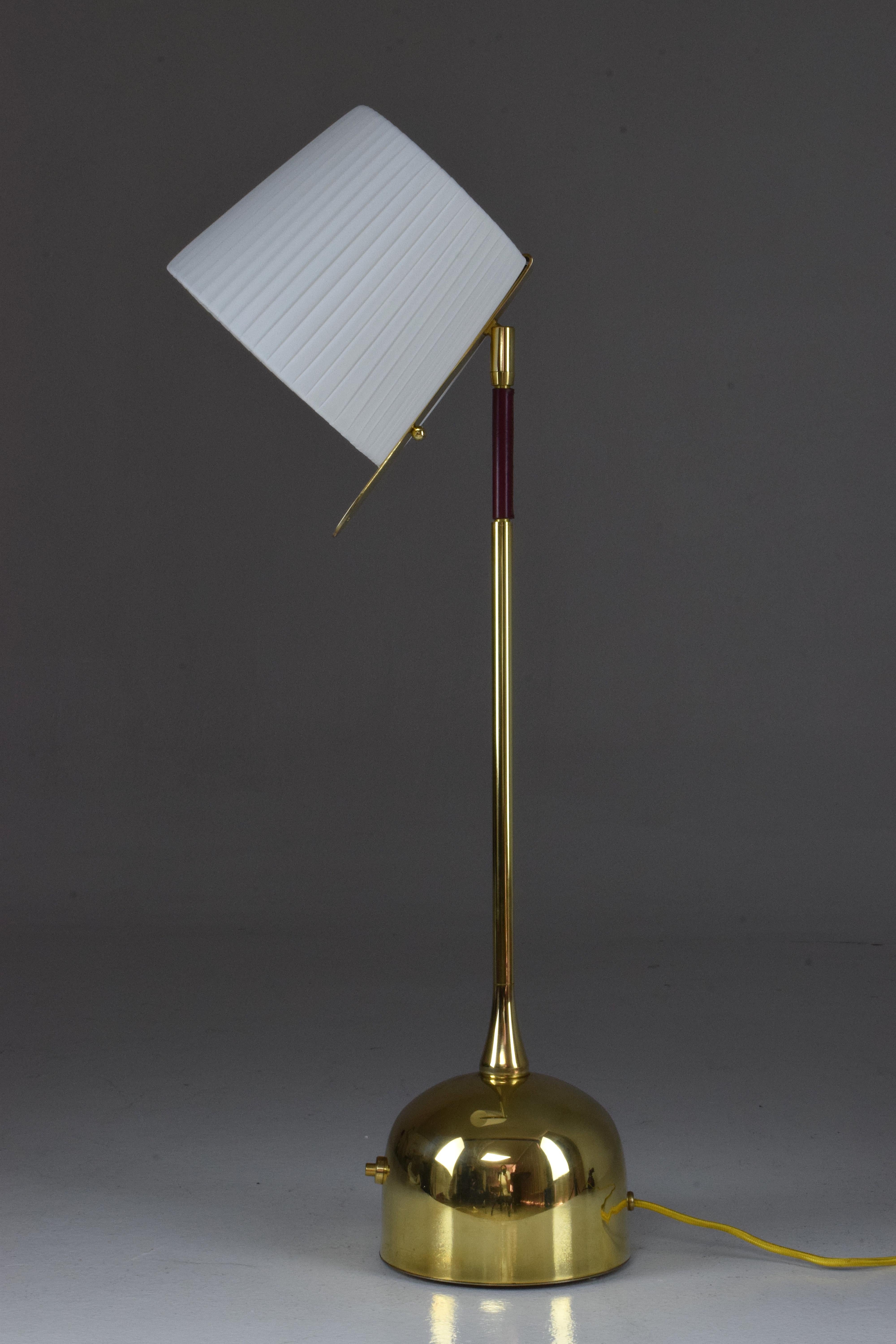 Contemporary handcrafted articulating table lamp pictured in a solid polished brass finish, adorned with a dark red hand-sewn sheathed leather detail by artisan saddle makers. The lamp is designed with our signature pear shaped joint and the