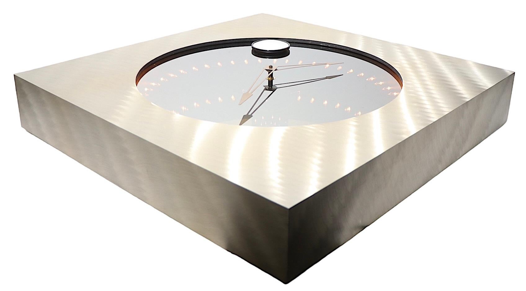 Chic, glam post modern infinity clock, mirror. The clock is surrounded by what appear to be receding points of light, hence the name Infinity Clock. The frame is constructed of brushed aluminum, with a dramatic circular glass face with the clock