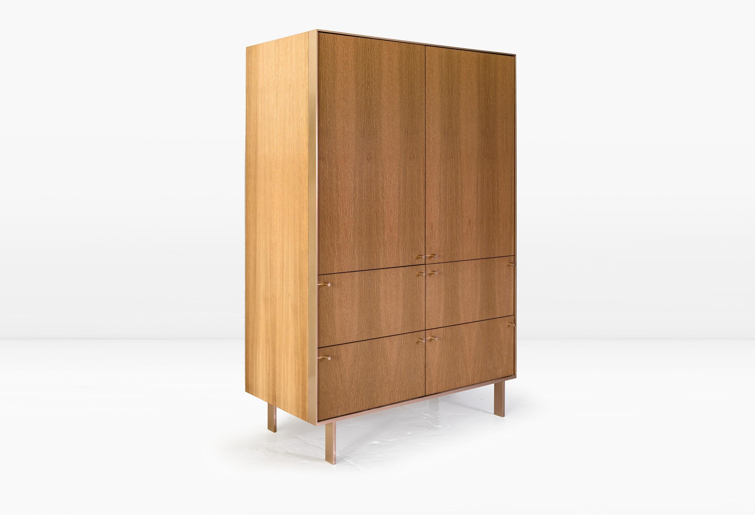 The quarter inch thick, metal strap which frames the Ingemar Cabinet, transforms into legs at the base while seamlessly marrying to the wood cabinet behind it. The back face of the unit’s interior is clad in optional black mirror and the adjustable