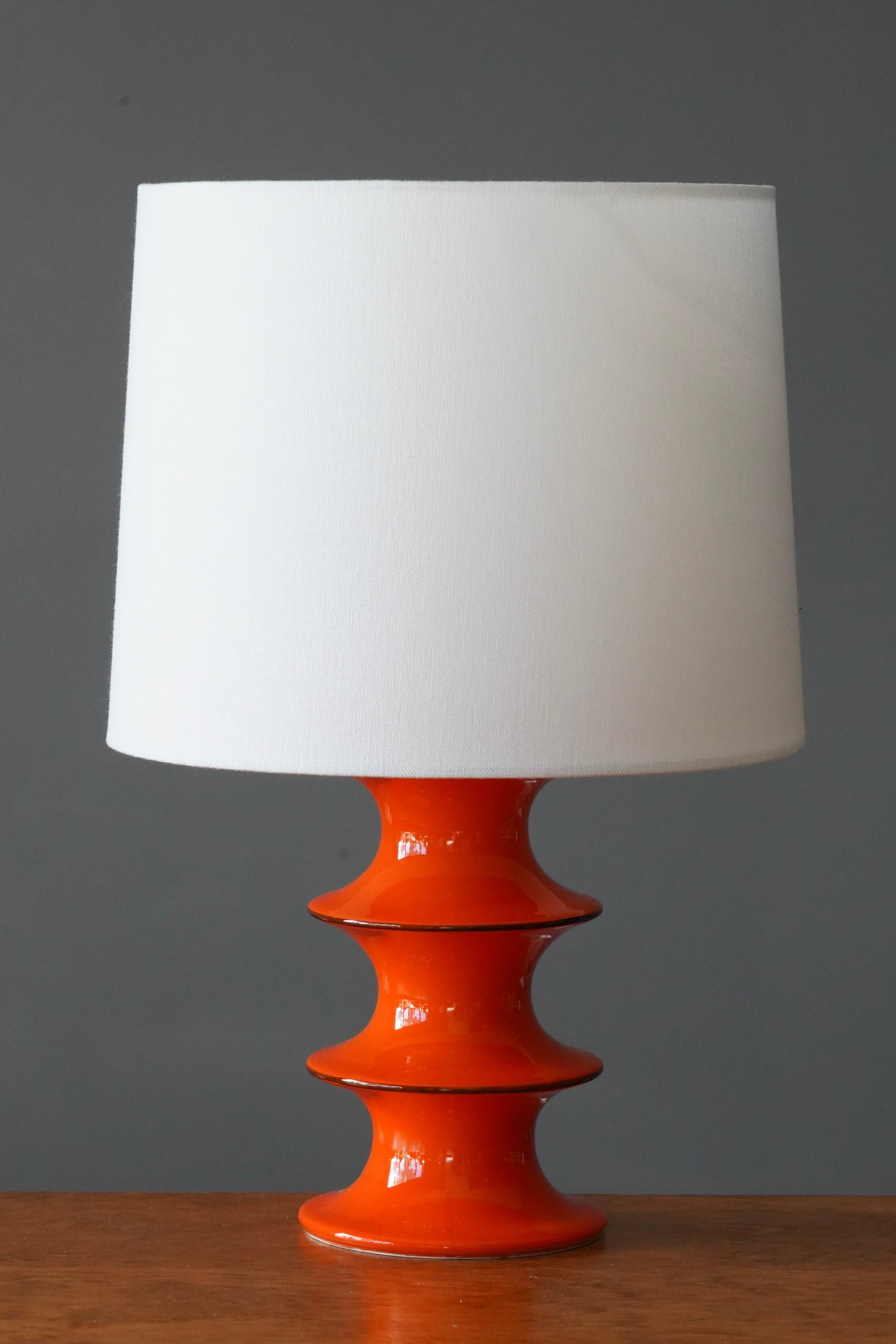 A table lamp designed by Inger Persson, produced by Rörstrand. Stamped. Orange glazed stoneware. c. 1960s.

Dimensions listed are without lampshade. 
Dimensions with shade: height is 15.5 inches, width is 10 inches.
Dimensions of shade: top