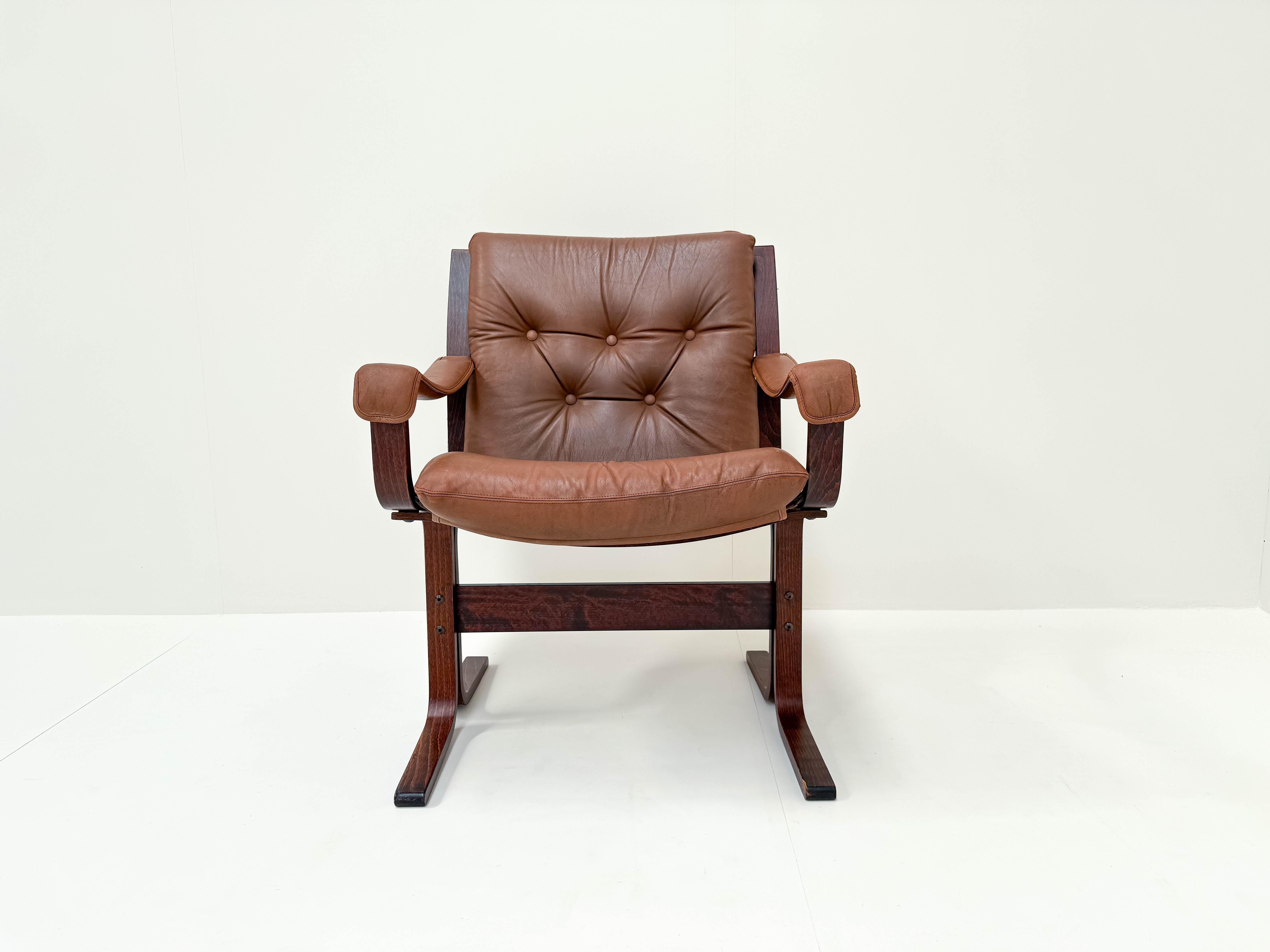 Questa iconica poltrona lounge, disegnata da Ingmar Relling per Westnofa, presenta una splendida struttura in palissandro laminato abbinata a un morbido rivestimento in pelle marrone. L'esclusiva struttura in palissandro laminato conferisce al pezzo