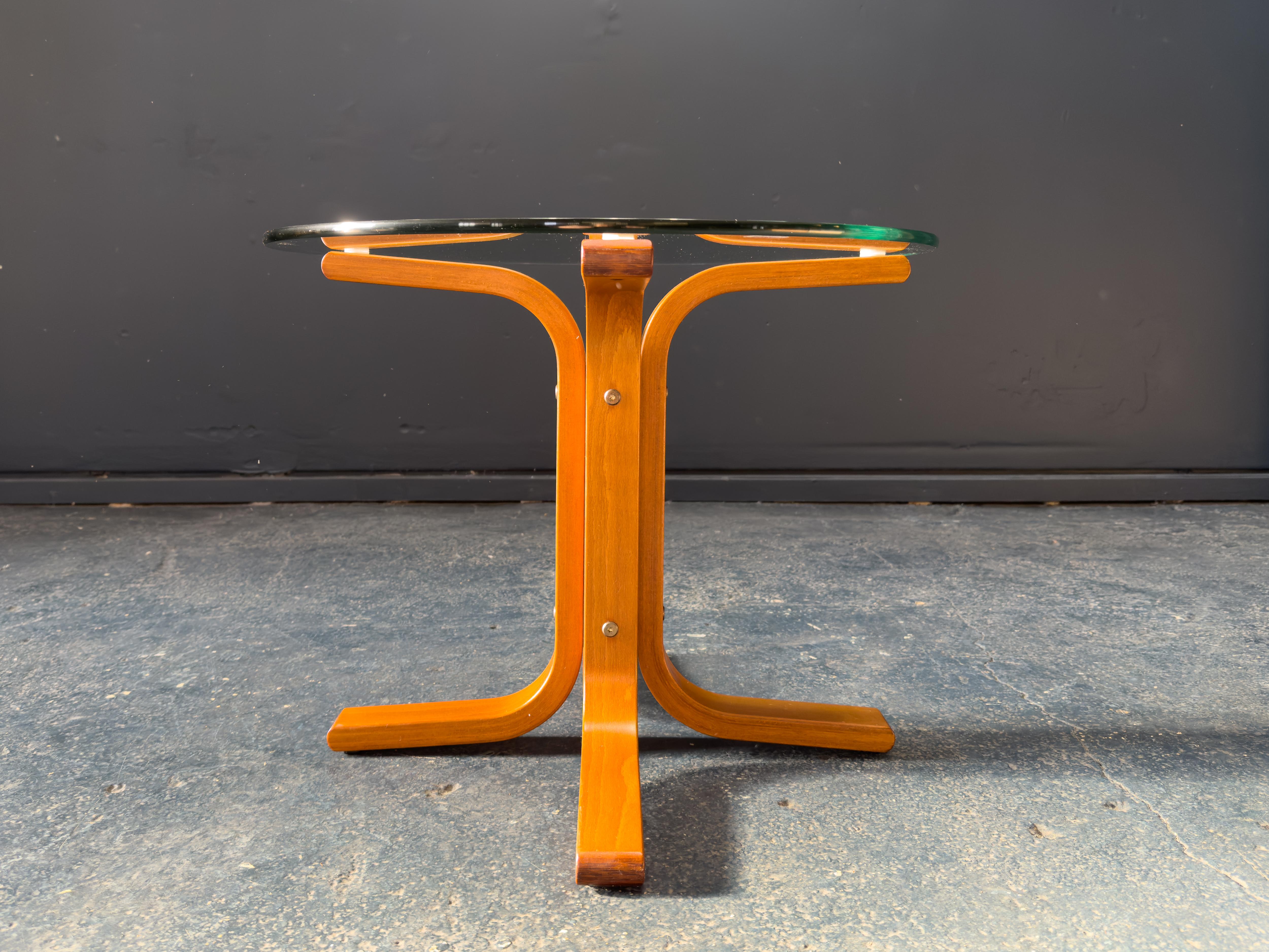 Cette table basse élégante et sculpturale du célèbre designer norvégien Ingmar Relling est une belle expression du design scandinave moderne. Associant un plateau en verre transparent à un piètement en bois de hêtre stratifié sculpté, la table