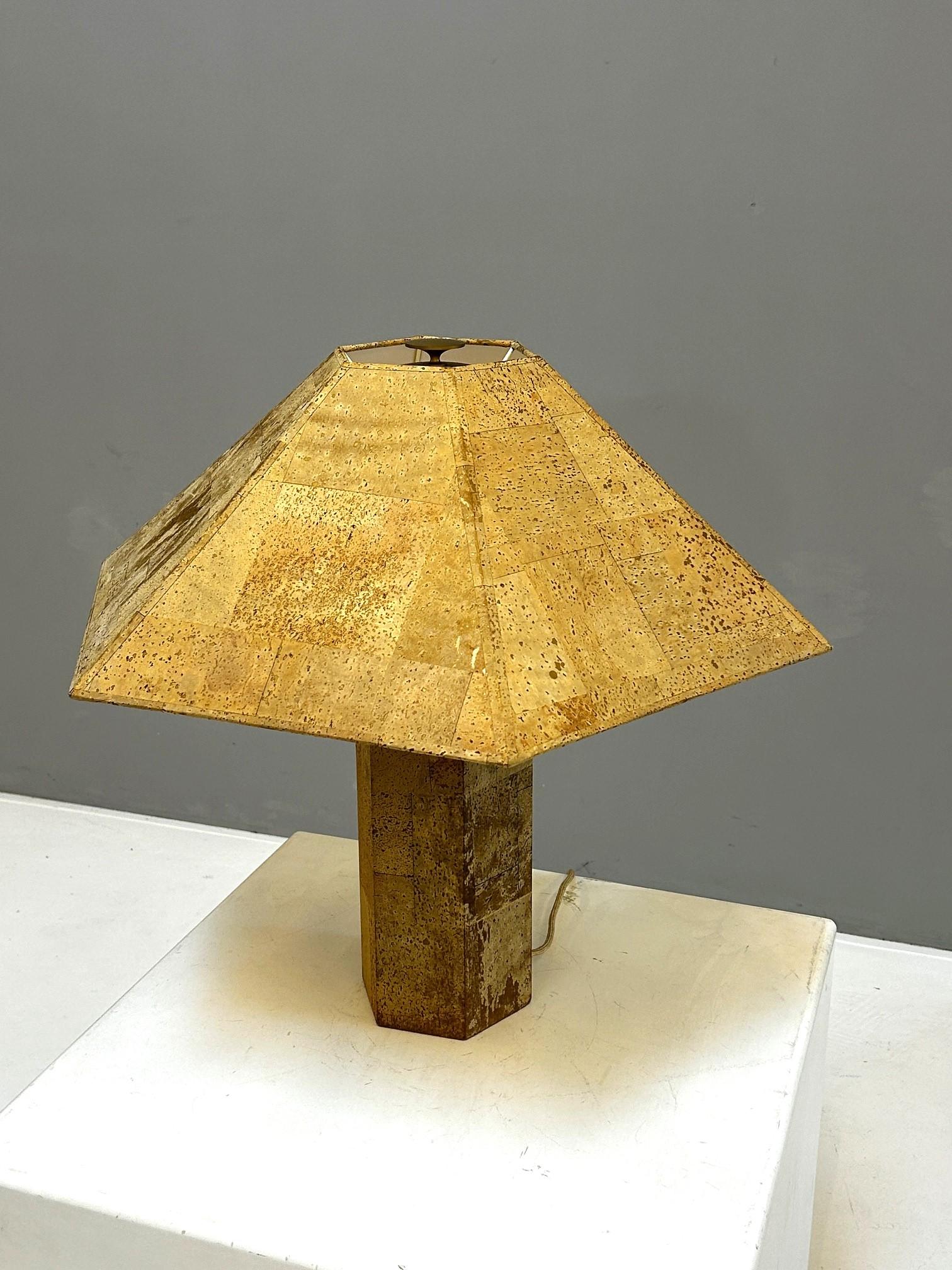 Table lamp with hexagonal shade and stem.
Entire lamp covered with natural cork.
The inside of the shade is covered with white plastic as a reflector.
Label by M Design.

Photo excerpt from an old Ingo Maurer sales catalog:
Illustration of a cork