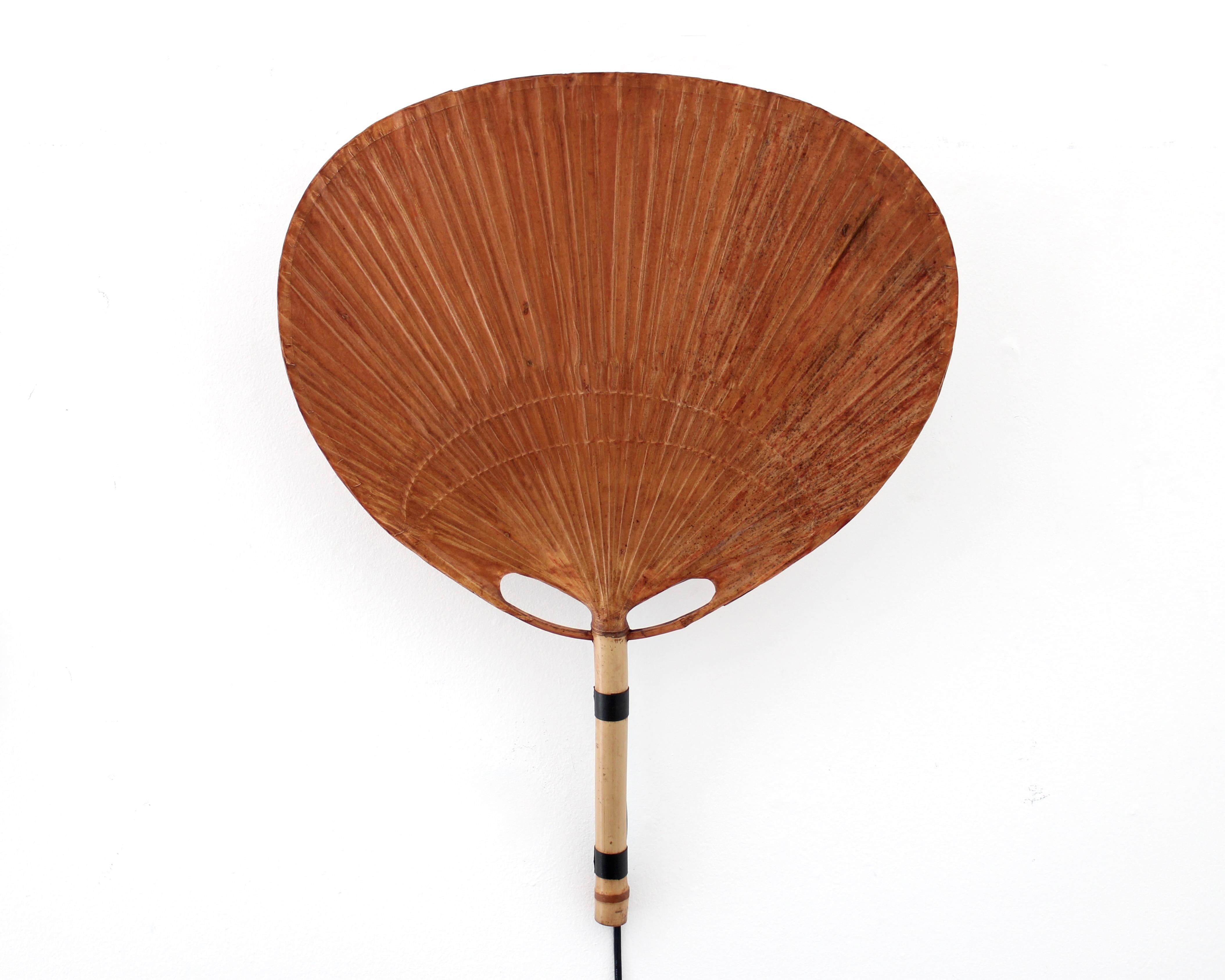 L'applique Uchiwa II d'Ingo Maurer est un exemple élégant du design des années 1970, avec une structure qui allie matériaux naturels et modernité. Le métal et le bambou sont harmonieusement combinés, tandis que le diffuseur en papier de riz laqué