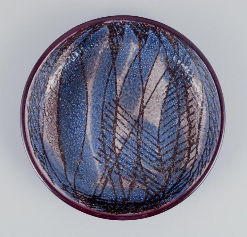 Ingrid Atterberg (1920-2008) for Upsala Ekeby, Sweden. 
Low ceramic bowl with an abstract design. 
Glazed in blue and sand-colored tones.
From the 1960s.
Stamped.
In perfect condition.
Dimensions: Diameter 21.0 cm x 3.5 cm.

Ingrid Atterberg is