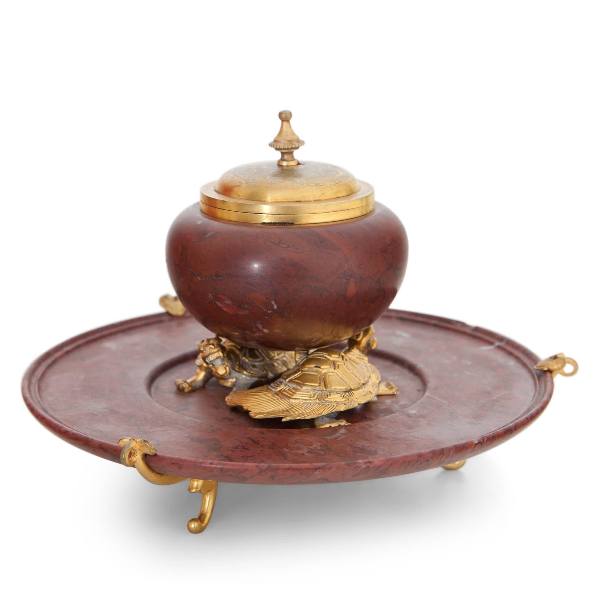 Inkwell out of red marble and gilt bronze by F. Barbedienne. The inkwell with a hinged lid stands on two bronze turtles and rests upon a three-legged marble plate. Maesures: Diameter inkwell barrel Ø 8 cm.