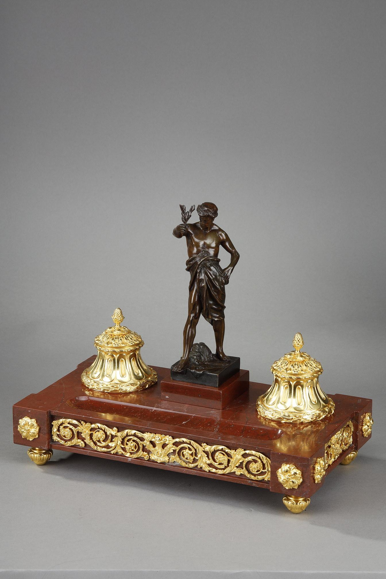 Encrier de bureau de style Louis XVI à base rectangulaire en marbre rouge orné de bronze ciselé et doré de rosettes et de guirlandes. Les seaux cannelés sont décorés de feuilles d'acanthe et de couronnes de laurier. Au centre se trouve une sculpture