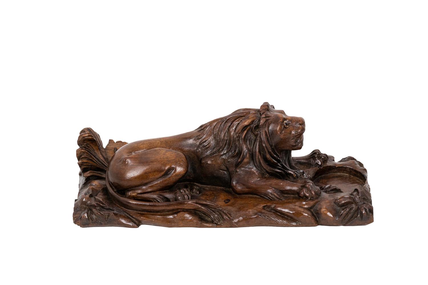 Inkwell in walnut figuring a lion lied down on a rock and foliage surface. In front of it, a circular hole to receipt the ink.

Work realized, circa 1880.