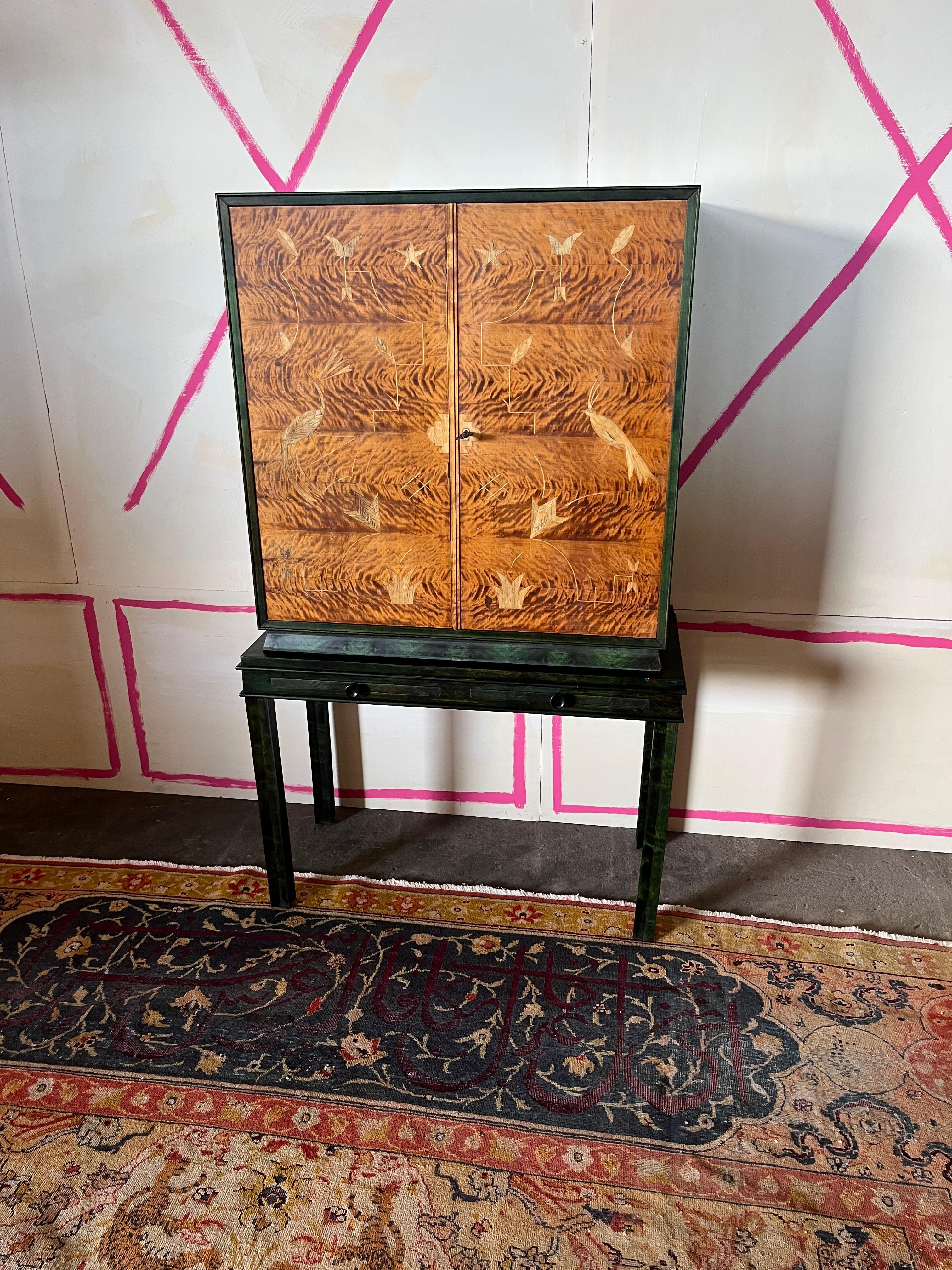 Un eccezionale mobile berlinese in stile Art Déco, del 1925 circa, impiallacciato in betulla fiammata tinta di verde e ambra con ante impiallacciate orizzontalmente e riccamente intarsiate in acero. L'intarsio presenta uccelli accanto a forme