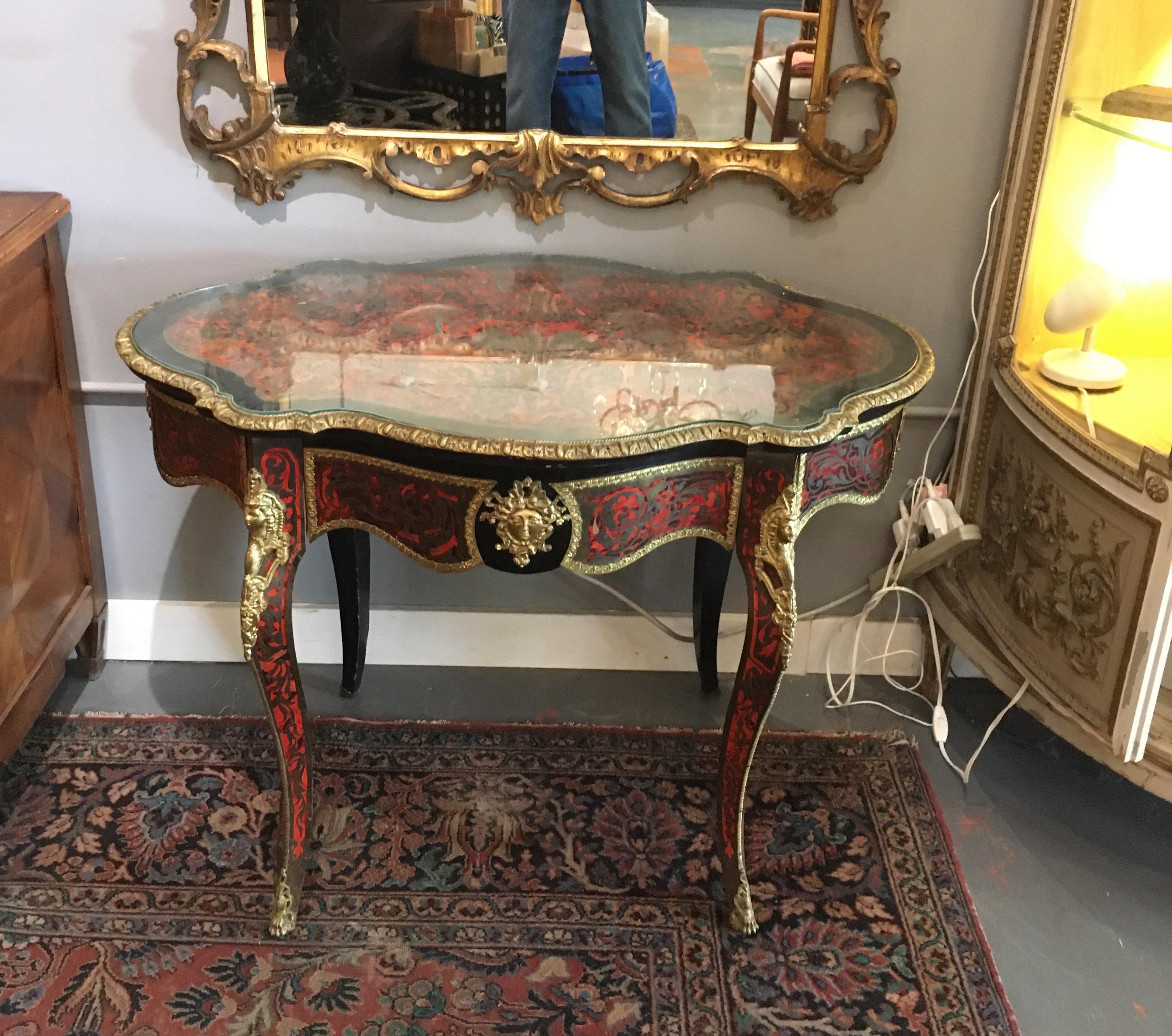 Lovely early 20th century inlaid Boulle serpentine shaped center table with gilded ormolu mounts on all sides. One drawer, raised on cabriole legs with ormolu mounts. Custom cut glass top follows serpentine shape.