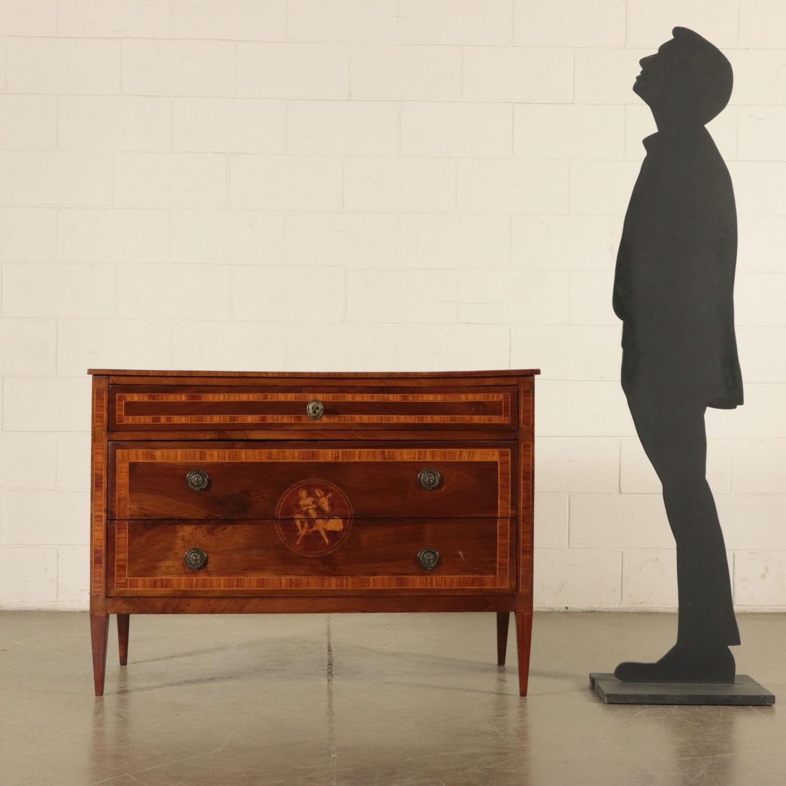 Inlaid chest of drawers supported by four truncated pyramidal feet; two frontal drawers surmounted by a third drawer in the band underneath the top. Walnut with marple and Brazilian rosewood inlays. Along the sides, inside two reserves, there are