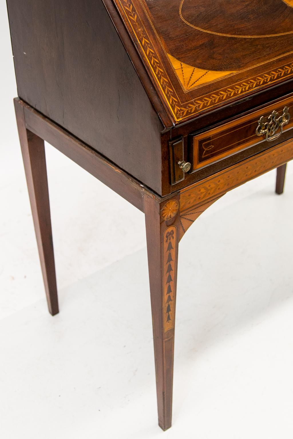 Inlaid English mahogany Hepplewhite Slant front desk on legs. It has quarter fans connected by boxwood string inlay. The fall board is inlaid with leaf and berry border. Ebony and satinwood herringbone inlay surround quarter fans and a central