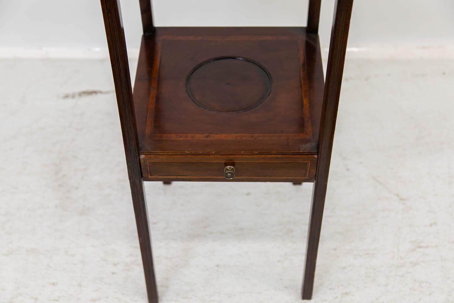 The top of this mahogany table has a molded bullnose edge and is banded with a satinwood and ebony border. There are quarter fans in the corners of the border and an oval shell paterie framed by a marquee inlay band. The lower shelf has an incised