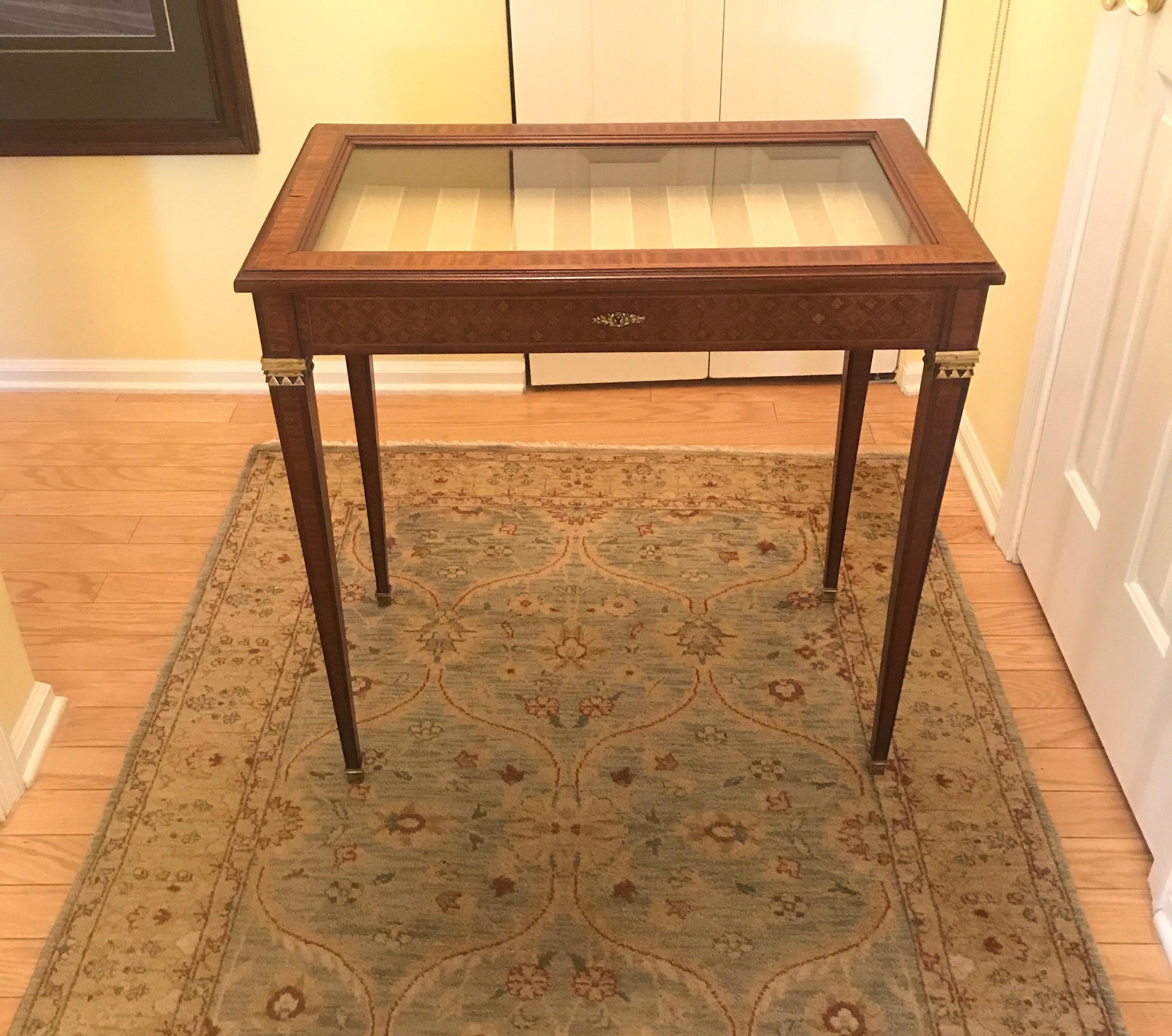 Elegant display table with mahogany with crossbanded inlay and marquetry inlaid sides. The glass display top supported by inlaid tapering legs with a satin broad stripe damask pad insert. Perfect to display a collection or jewelry in excellent well
