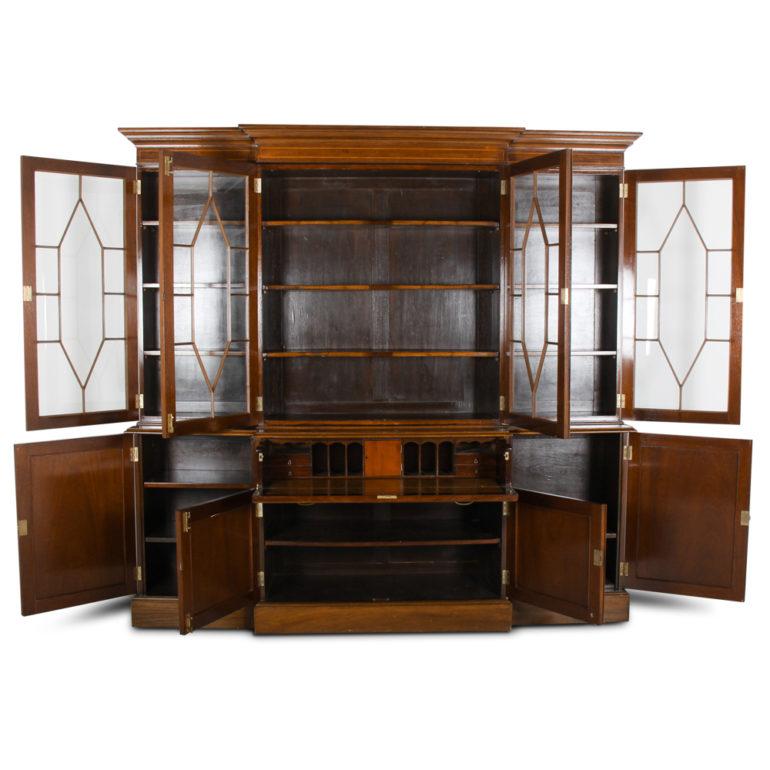 An English Georgian Revival breakfront bookcase in mahogany with four upper glazed doors opening to reveal adjustable shelves and four lower cabinets. A central drawer opens and drops down to provide a secretary work space with cubbyholes, small