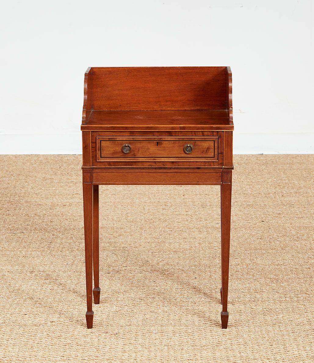 A small occasional or hall table having a rectangular top with three-sided raised surround with scalloped sides on a drawer with double brass ring pulls above a plinth apron, standing on tapered square section legs ending in spade feet.  Mahogany