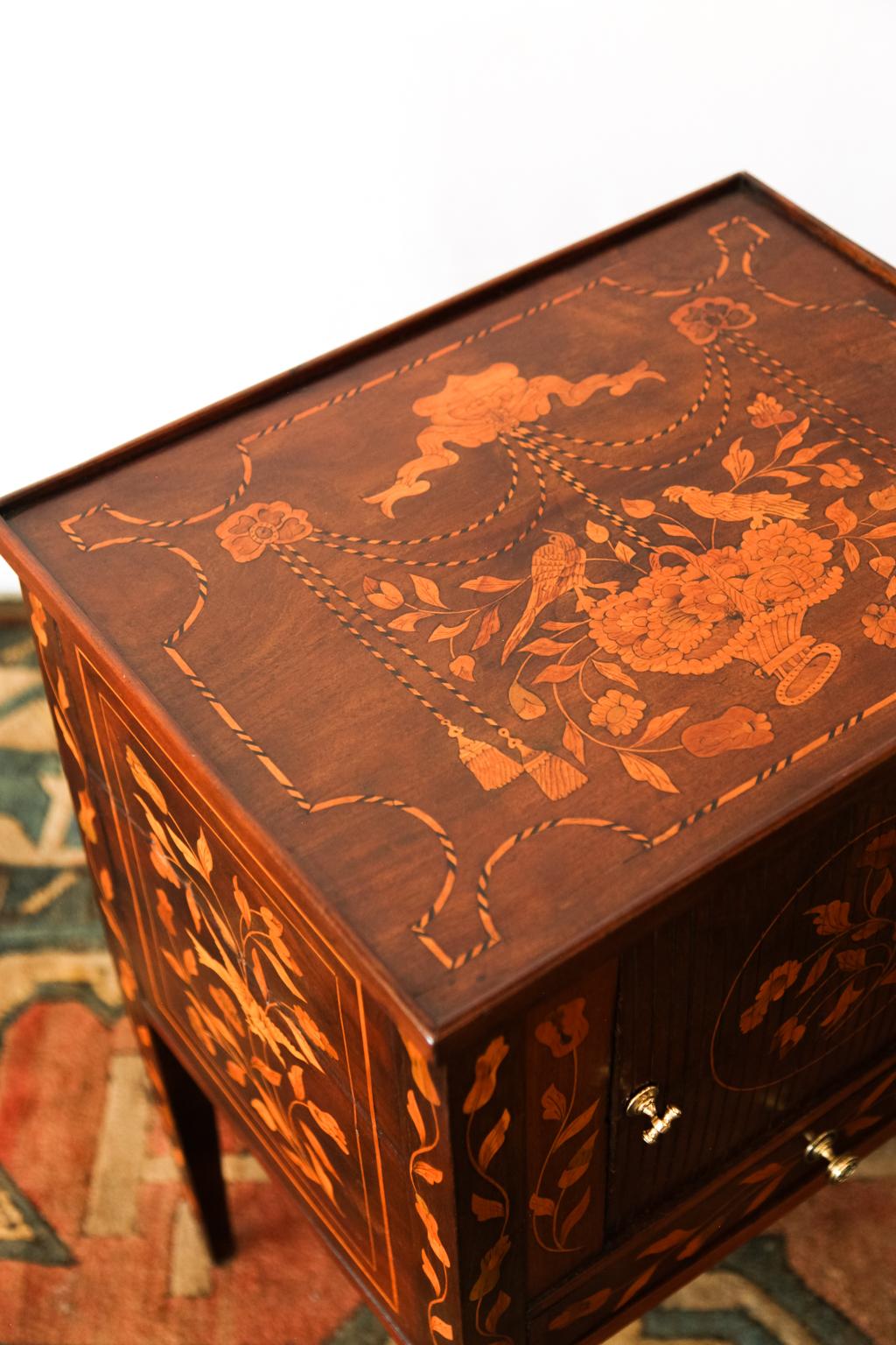 Inlaid marquetry one-drawer commode with boxwood and ebony inlay and baskets of flowers and birds. The wood is walnut and has inlaid rope swags terminating in tassels. The door is simulated tambour, but is solid.
