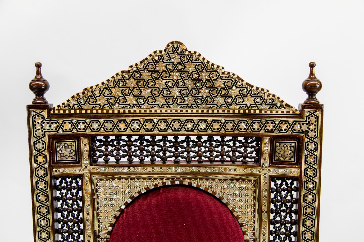Inlaid Moroccan armchair, is profusely inlaid with bone and mother of pearl inlays in geometric patterns. The panels have interlaced ball and stick carvings. The top of the arms are inlaid with ebony and bone in stylized arabesque patterns.