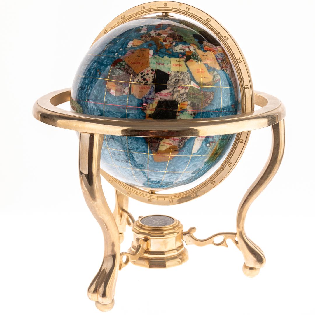 Cet exquis globe terrestre de bureau en Pietra Dura et laiton incrusté, attribué au célèbre fabricant Maitland-Smith, est un véritable chef-d'œuvre d'artisanat et de design. Le globe présente des pierres vibrantes, taillées à la main et incrustées