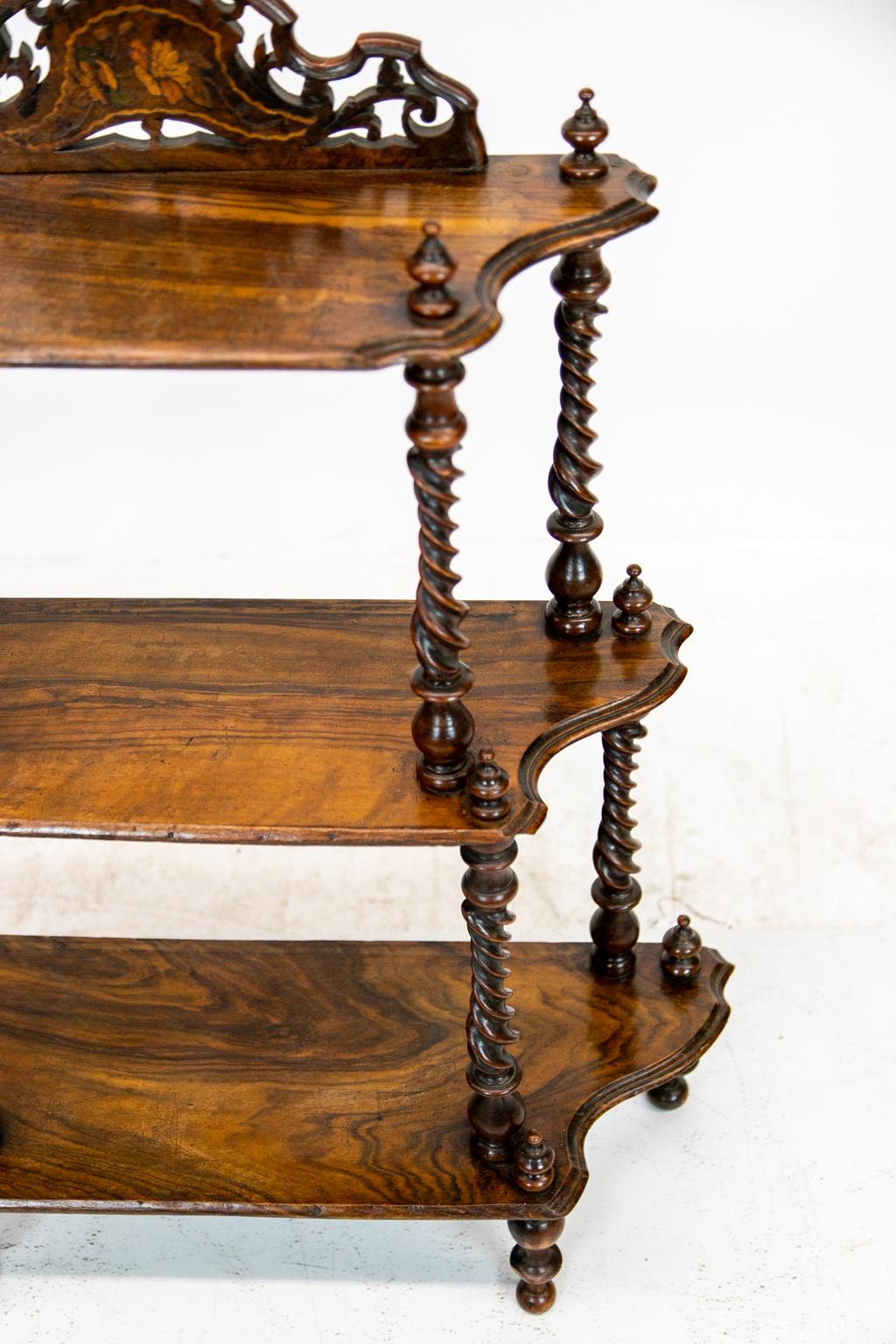 Inlaid rosewood three-tier shelf, with upright finials and barley twist support columns, it has shaped scalloped sides. There is floral inlaid pierced work on the crest, standing on turned legs.
        