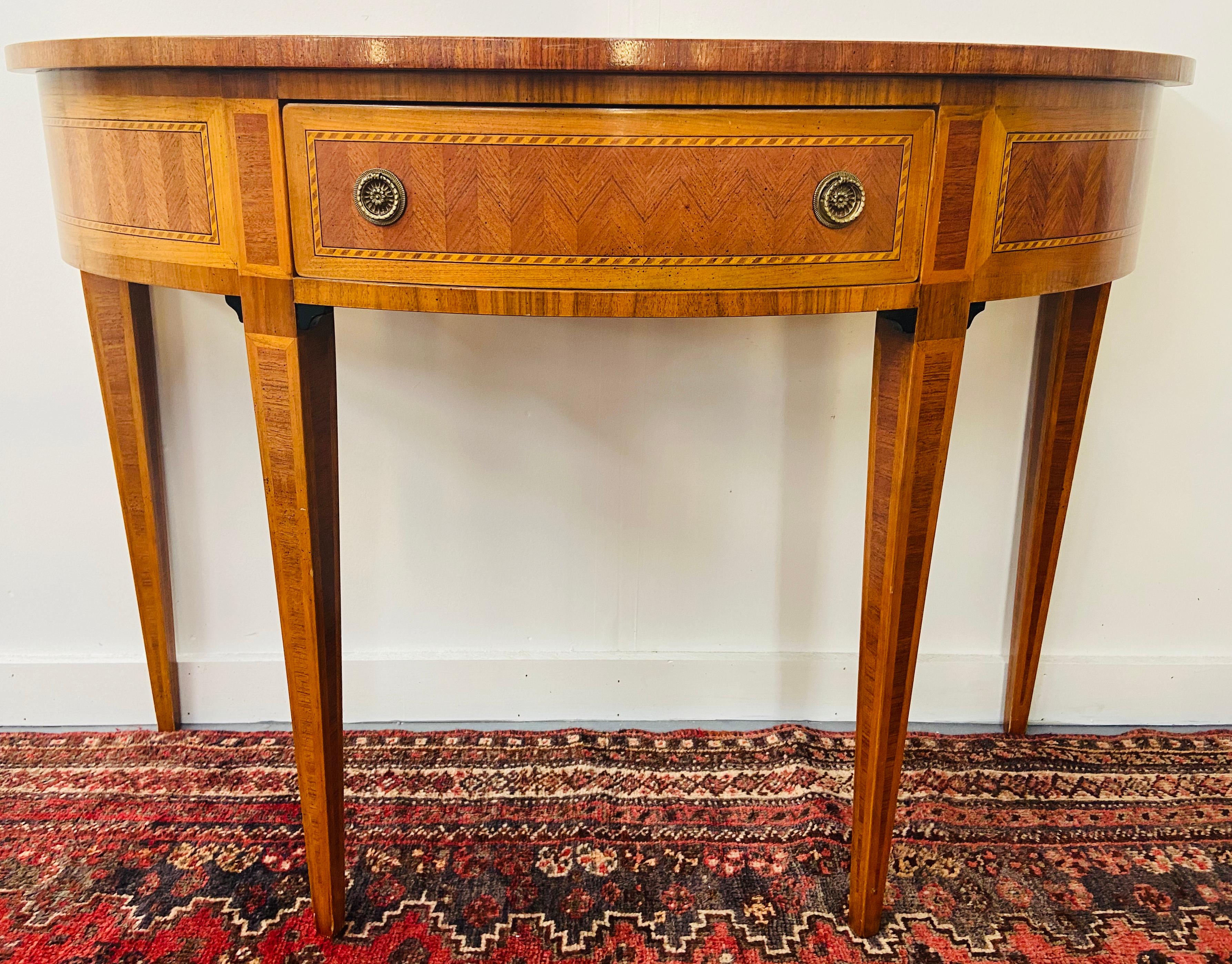 An elegant inlaid satinwood demilune console table with one middle drawer and original brass hardware. The console's timeless design is attributed to Maitland Smith. 
Some fading to the top of the table as shown on the pictures. 

Dimensions: