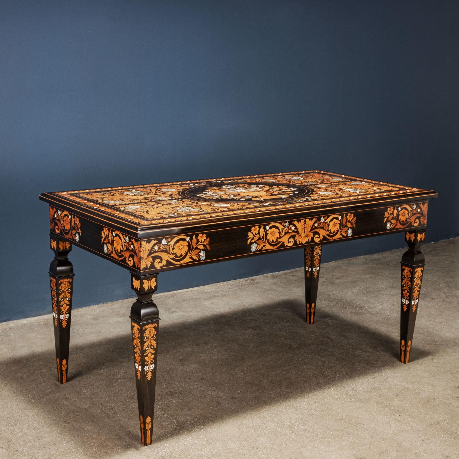 Rectangular table made of chestnut wood veneered in dark walnut and inlaid with various woods, mother of pearl and bone. The inlay with floral motifs presents the top starting from four mirror reserves created around the central oval reserve where a