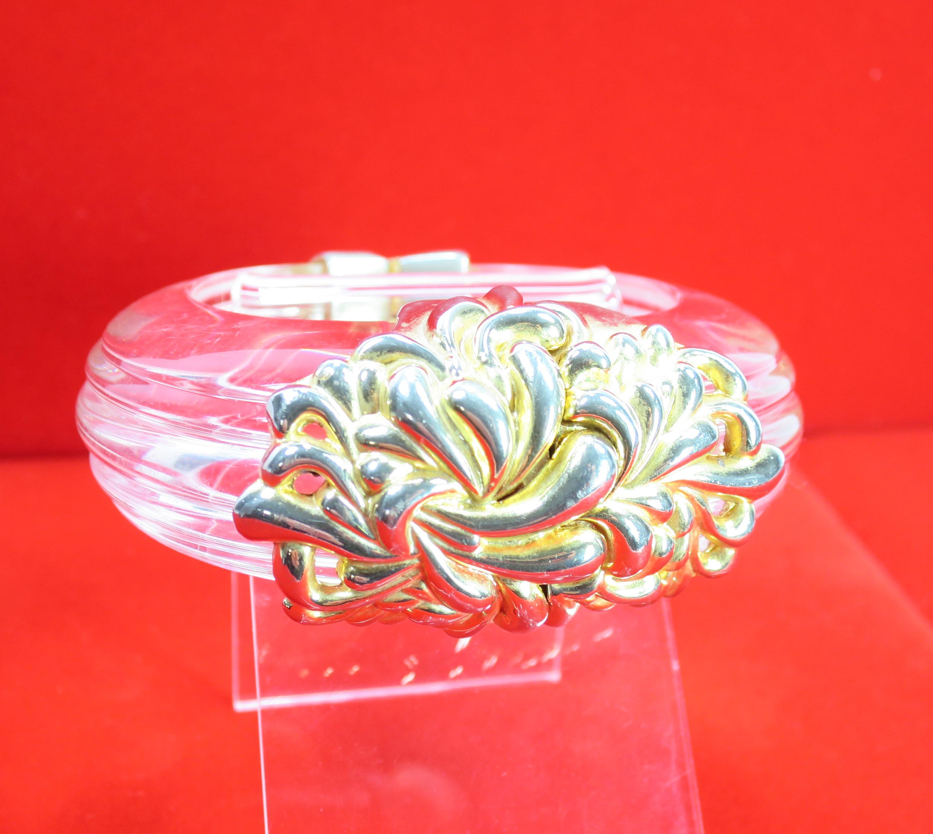 Offered here is a massive runway Lucite gilded hinged clamper bangle bracelet by Inna Cytrine Paris from the 1980s. Two huge halves of carved ribbed and tapered clear Lucite are joined by a gilded arabesque design centerpiece with an invisible