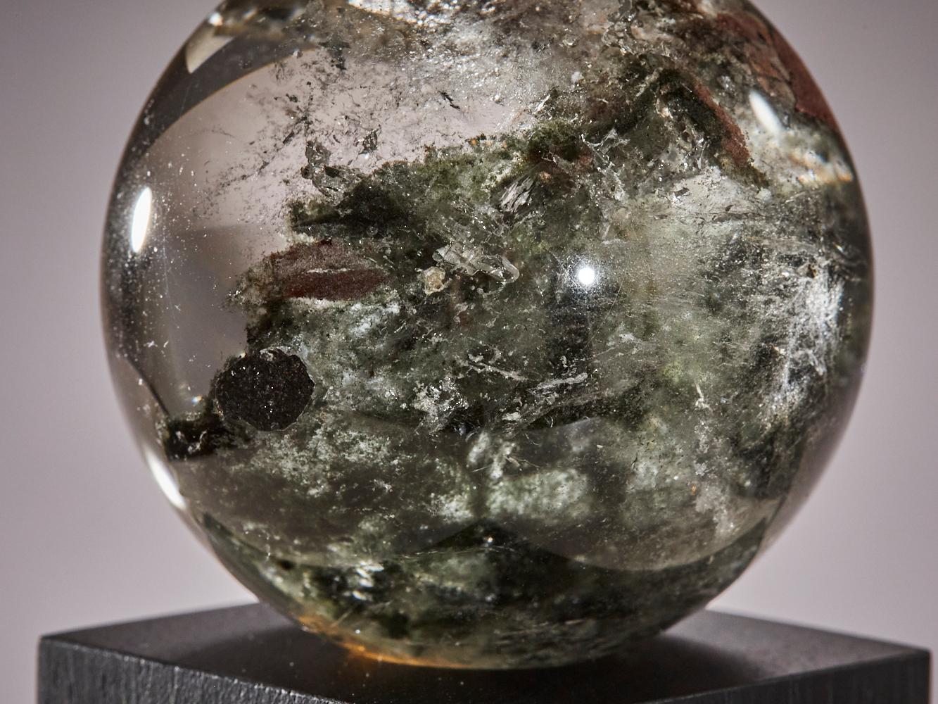 Cette étonnante sphère de quartz de Zambie révèle un monde caché à l'intérieur.
Depuis sa surface claire, vous pouvez voir des formations minérales uniques qui s'élèvent
comme de petites montagnes. Au centre, un second cristal semble flotter dans le