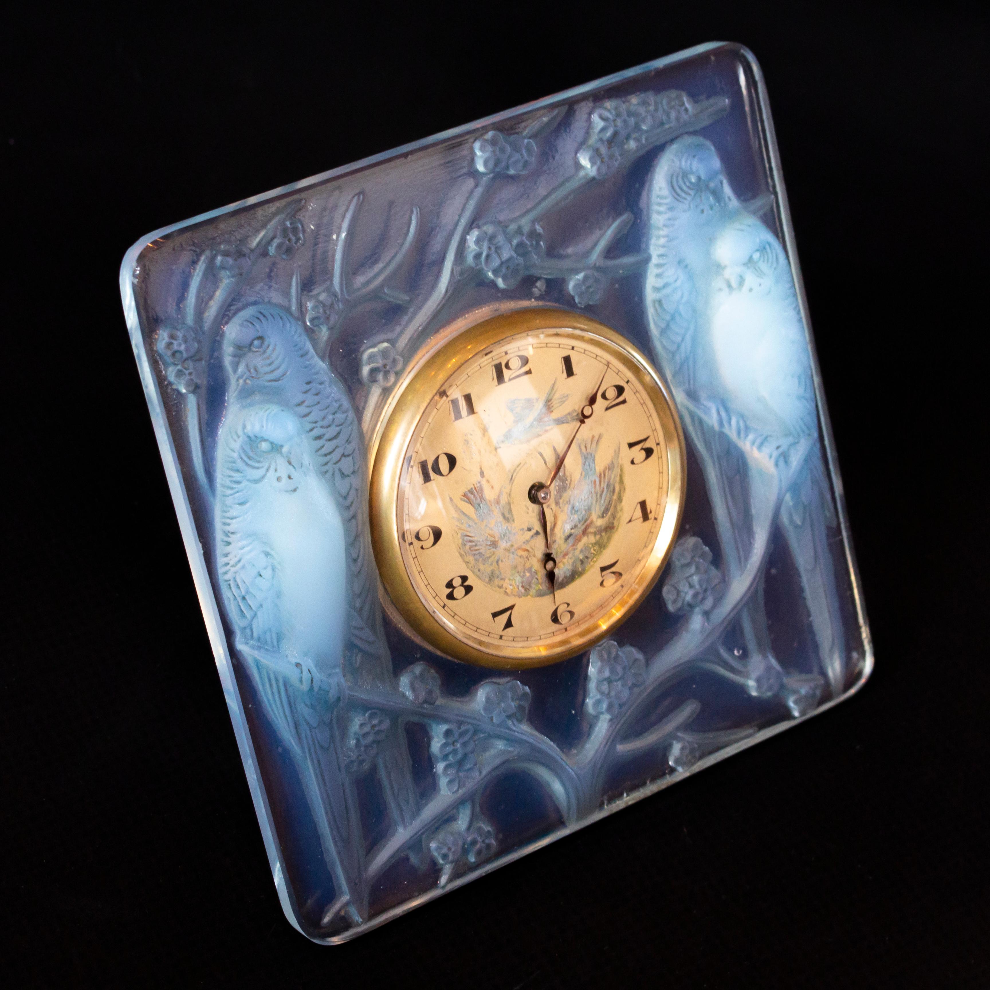 Inséparables, an Art Deco glass clock. Moulded in relief with two pairs of frosted lovebirds with original turquoise highlights, seated on prunus blossom. Hand painted clock face. Eight day Swiss movement and numbered, hinged stand.

Raised R