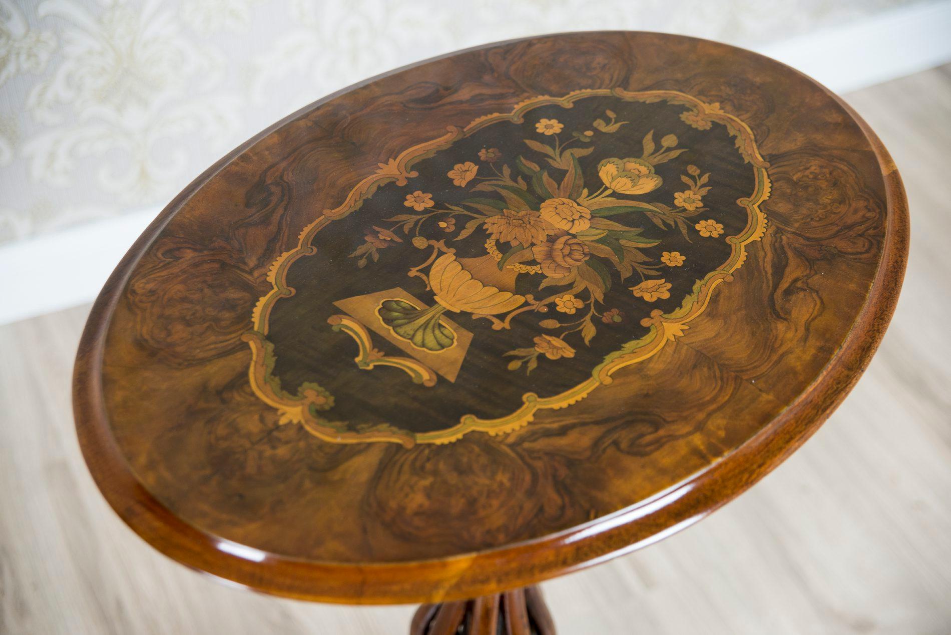 We present you an English tea table, circa 1860, with a lowered table top.
The top is oval, supported on a leg that is made of a bunch of wooden, bent bars that finish with a tripod.
Moreover, the tabletop is decorated with a beautiful