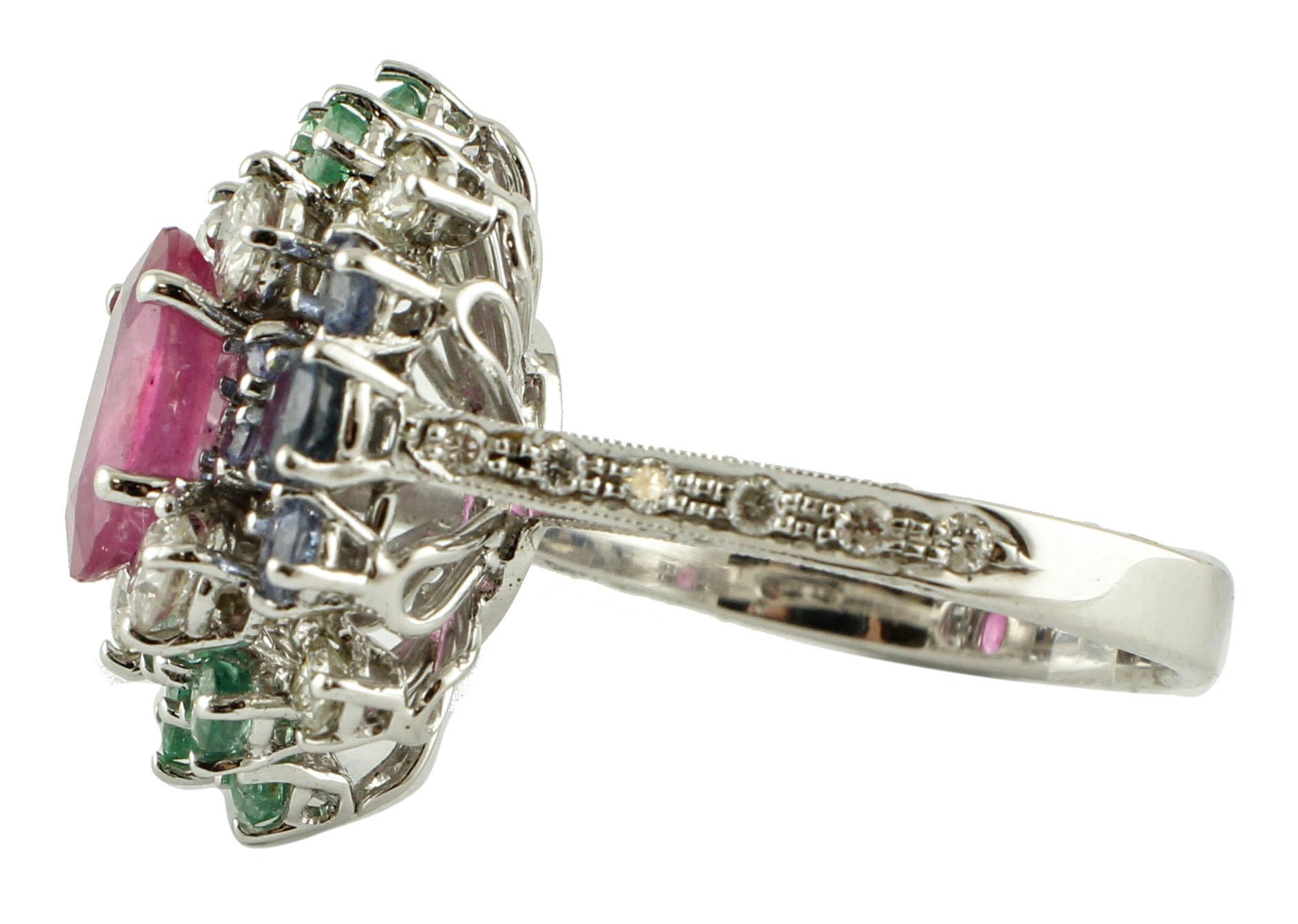 Magnifique bague à grappe en or blanc 14k, montée avec un rubis central, entouré de beaux diamants brillants, d'émeraudes et de saphirs bleus clairs. 
Cette bague est entièrement réalisée à la main par des maîtres orfèvres italiens. 
Diamants 0,96