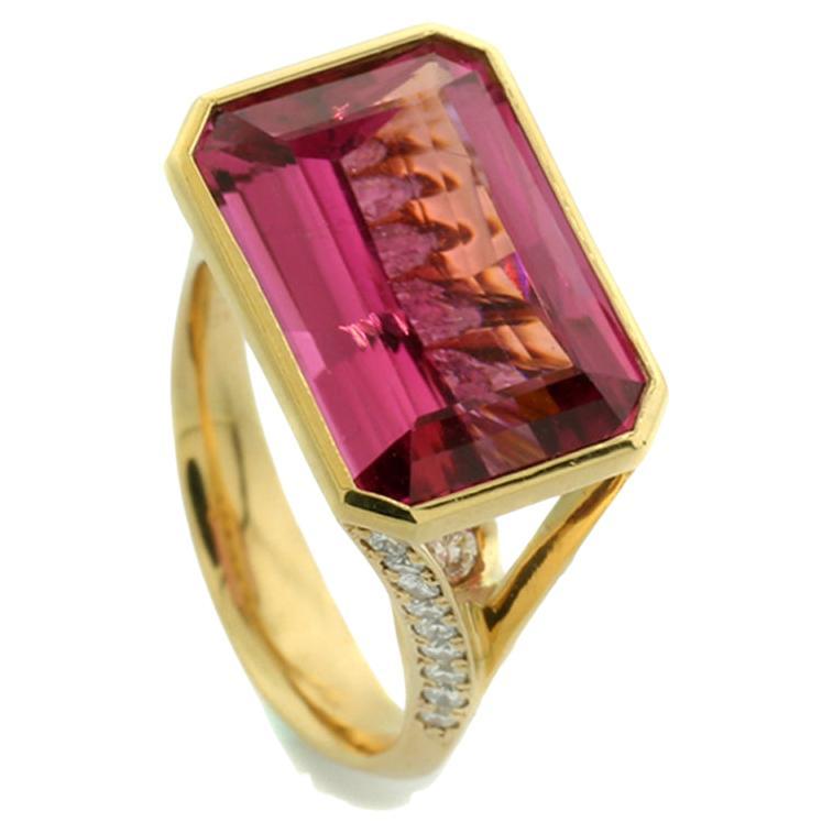 a tourmaline approx. 8.46 carat, intense Pink, eye-clean, emerald cut, set in an octagonal bezel. The high bipartite v-shaped ring shoulders are set with brilliant cut diamonds, the ring band passing under the 