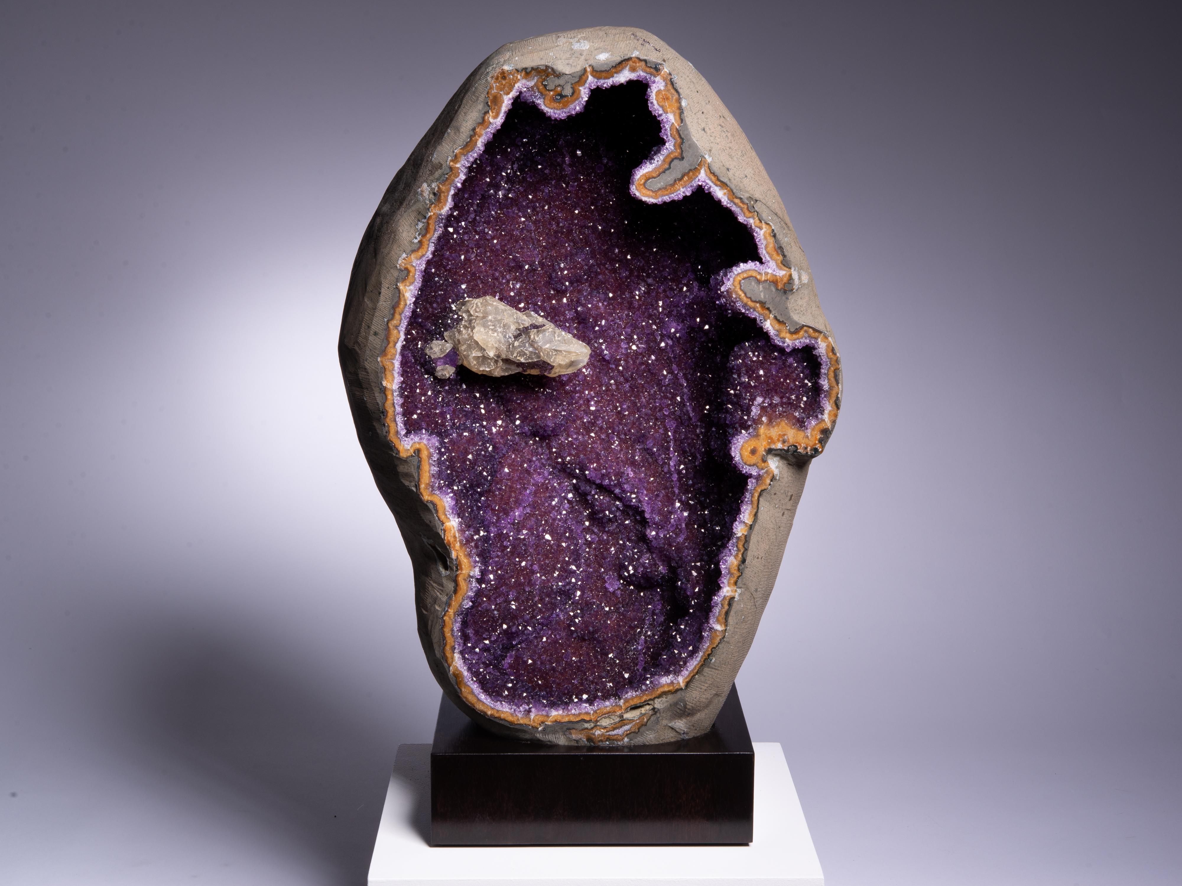 This split geode reveals incredibly intense amethyst with a calcite to the
upper left. The almost impossibly intense colour is a product of the
rich amethyst overlaid on a bed of unusual orange agate. The exterior
smoothed basalt.

This piece